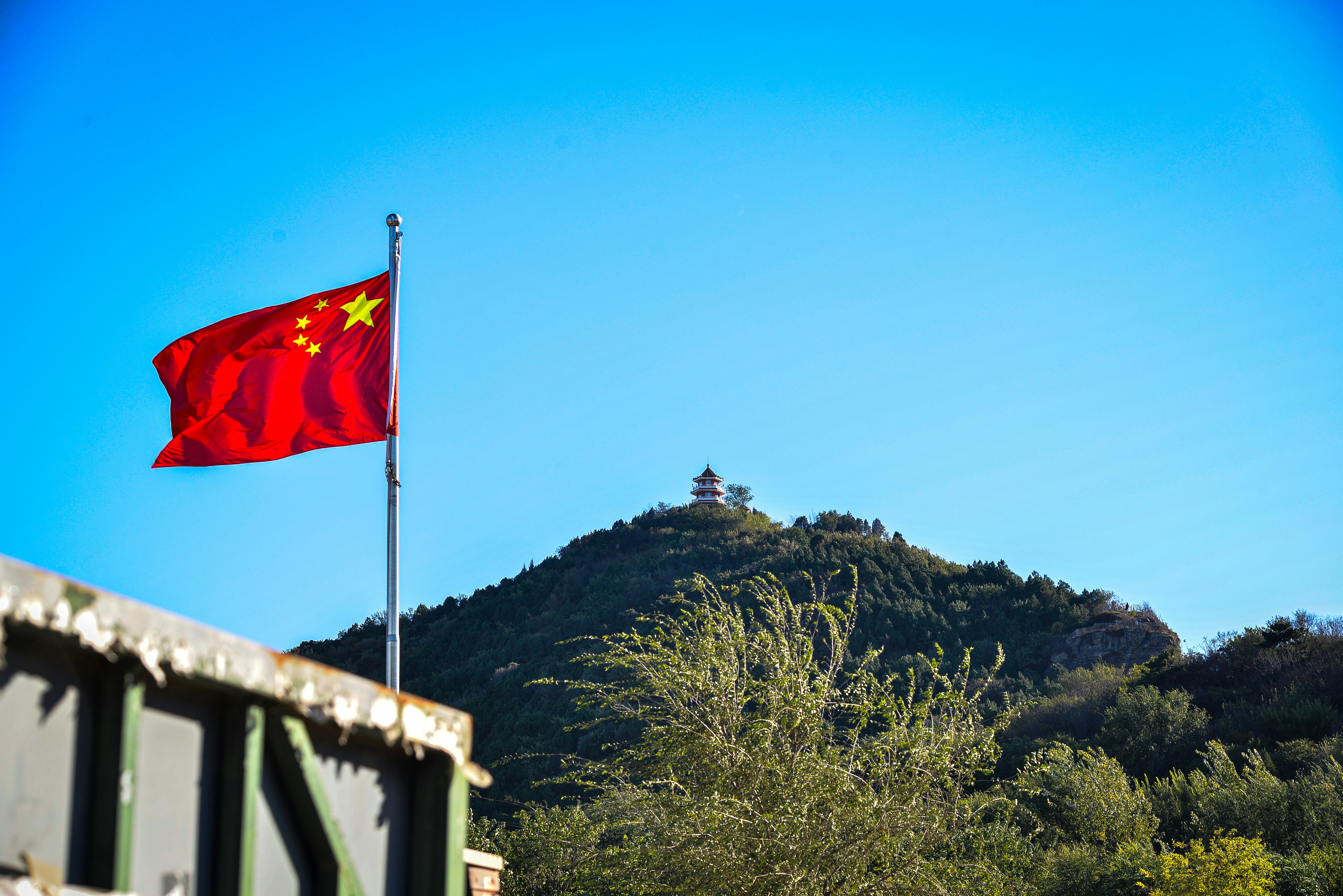 Chinese flag flying on a pole with a mountain.