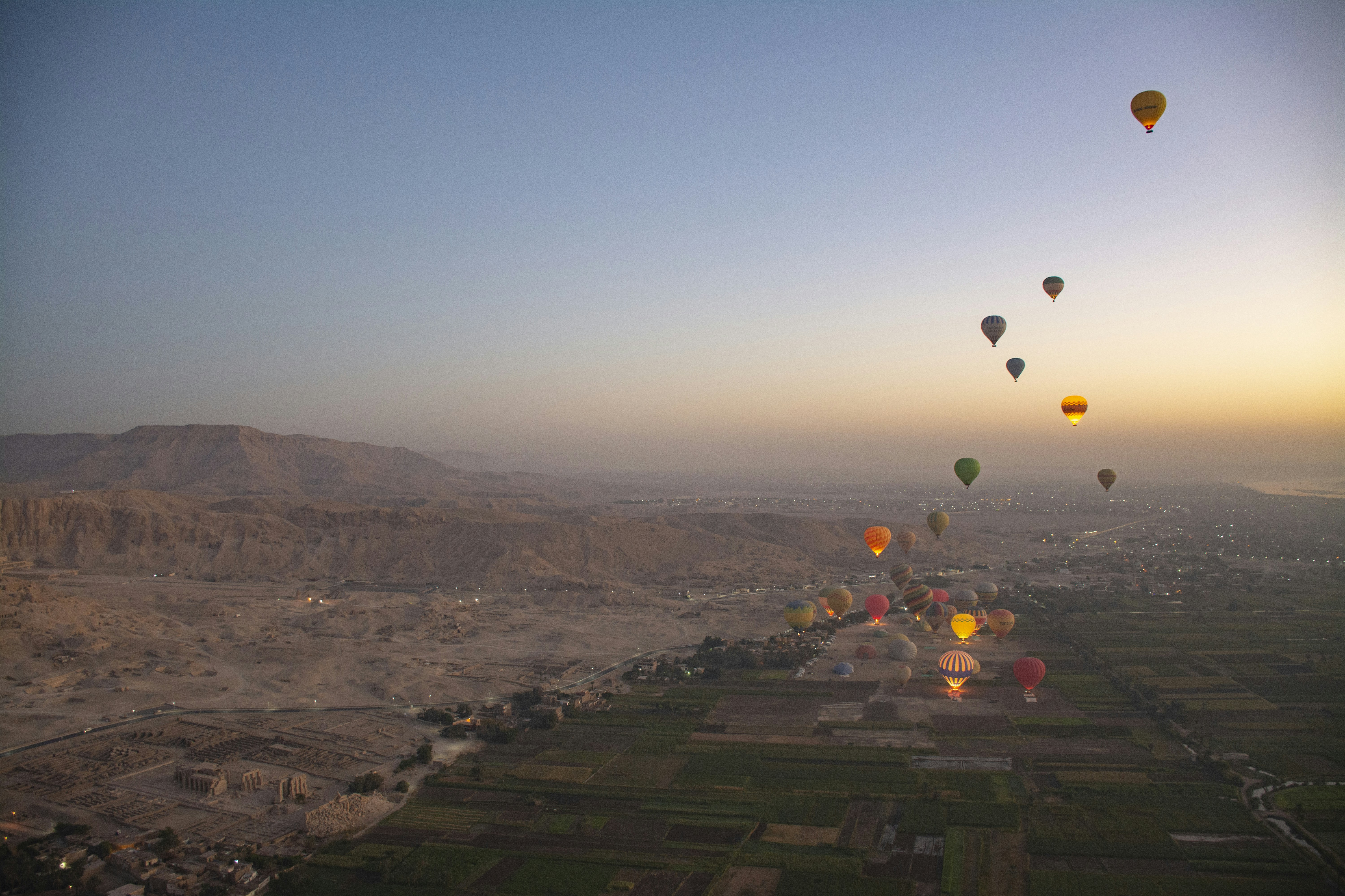 Hot air balloons float over a river valley at sunrise.