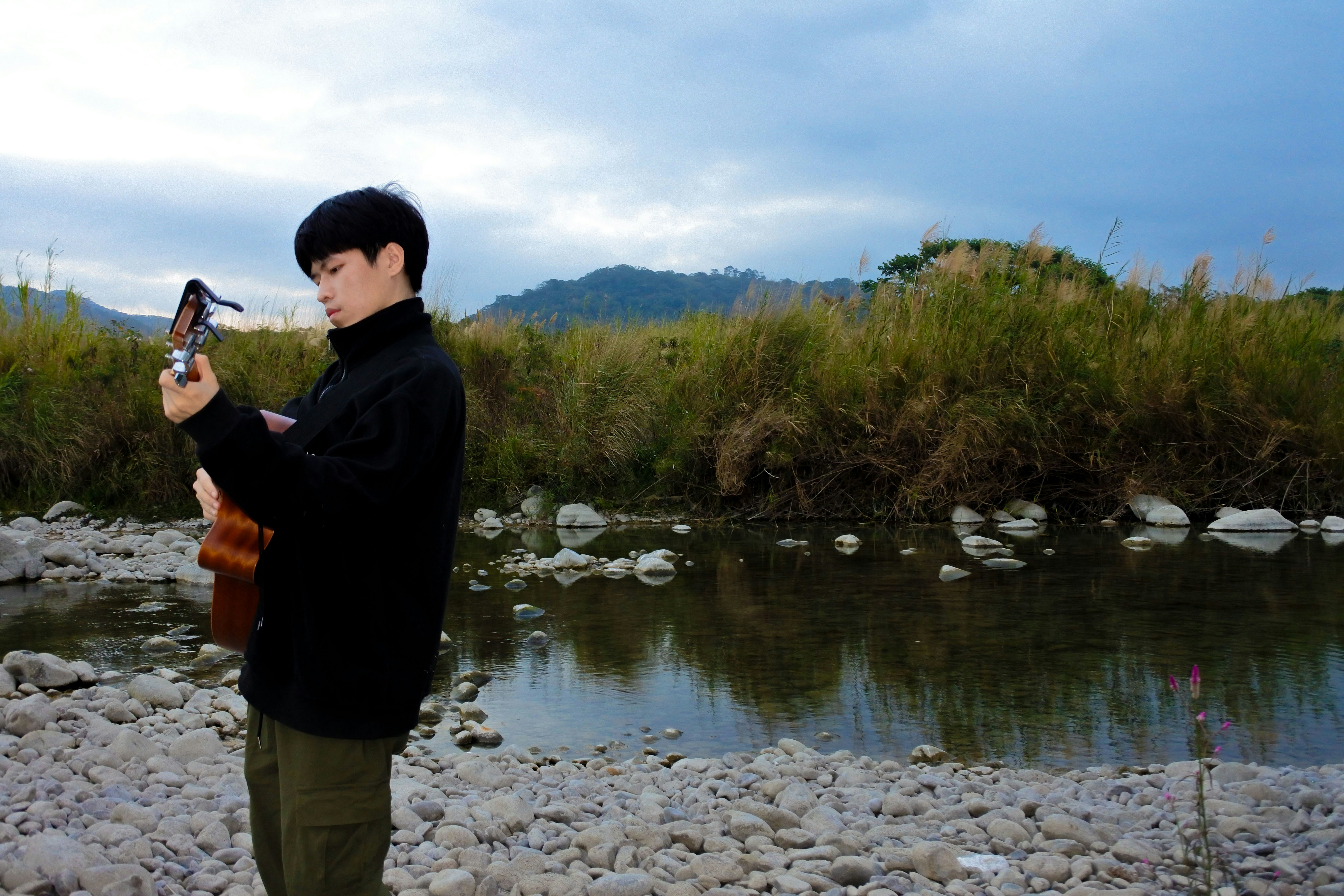 Man playing ukulele by a rocky riverbank