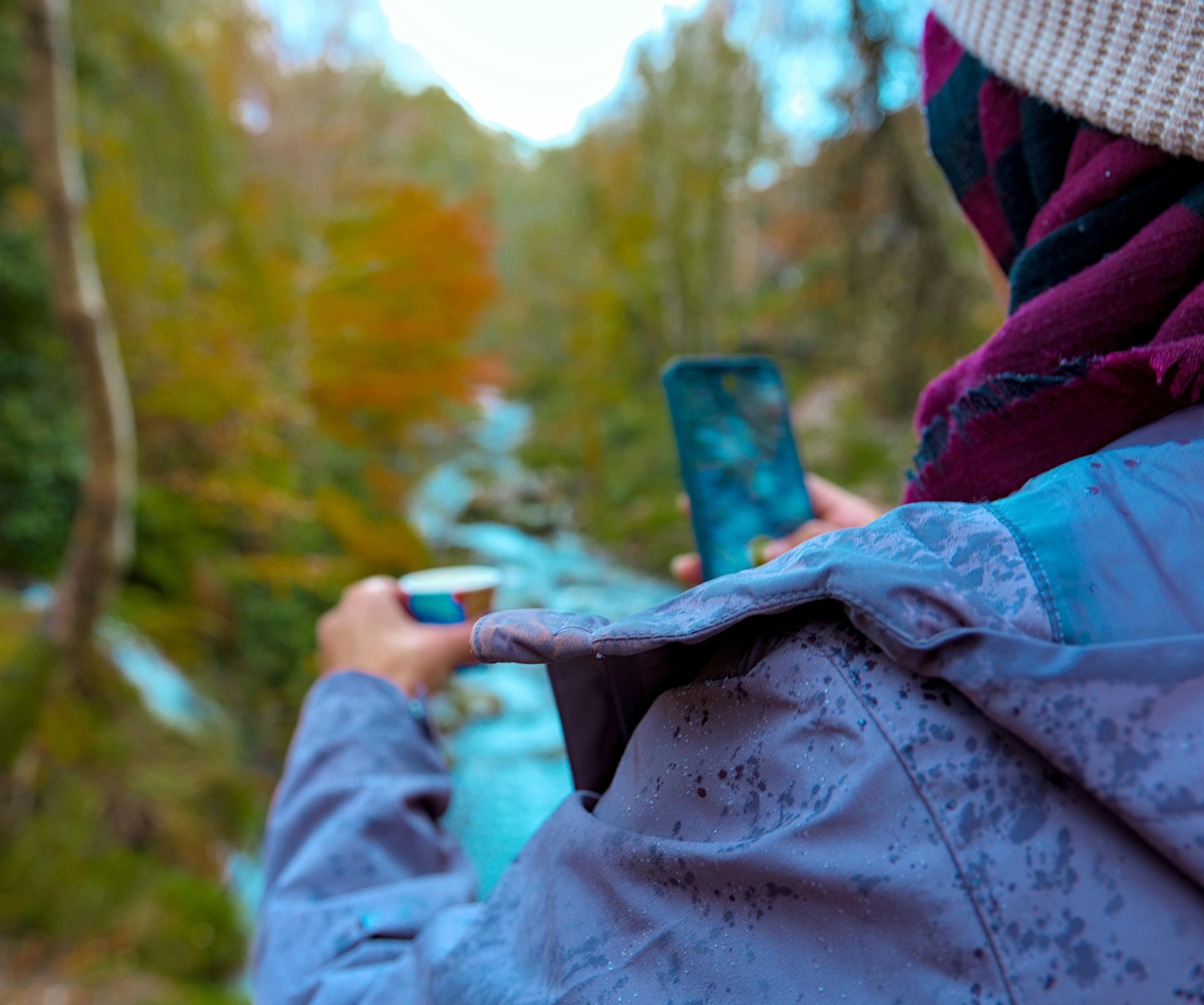 Person mit Tasse und Telefon in der Nähe des Flusses