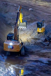 Two excavators working on a construction site at night.