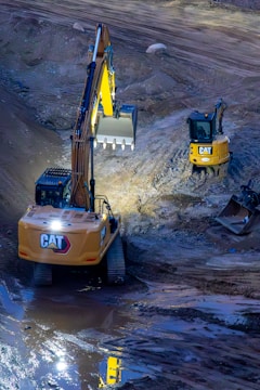 Two excavators working on a construction site at night.
