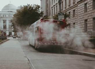 Red bus emitting smoke on a city street