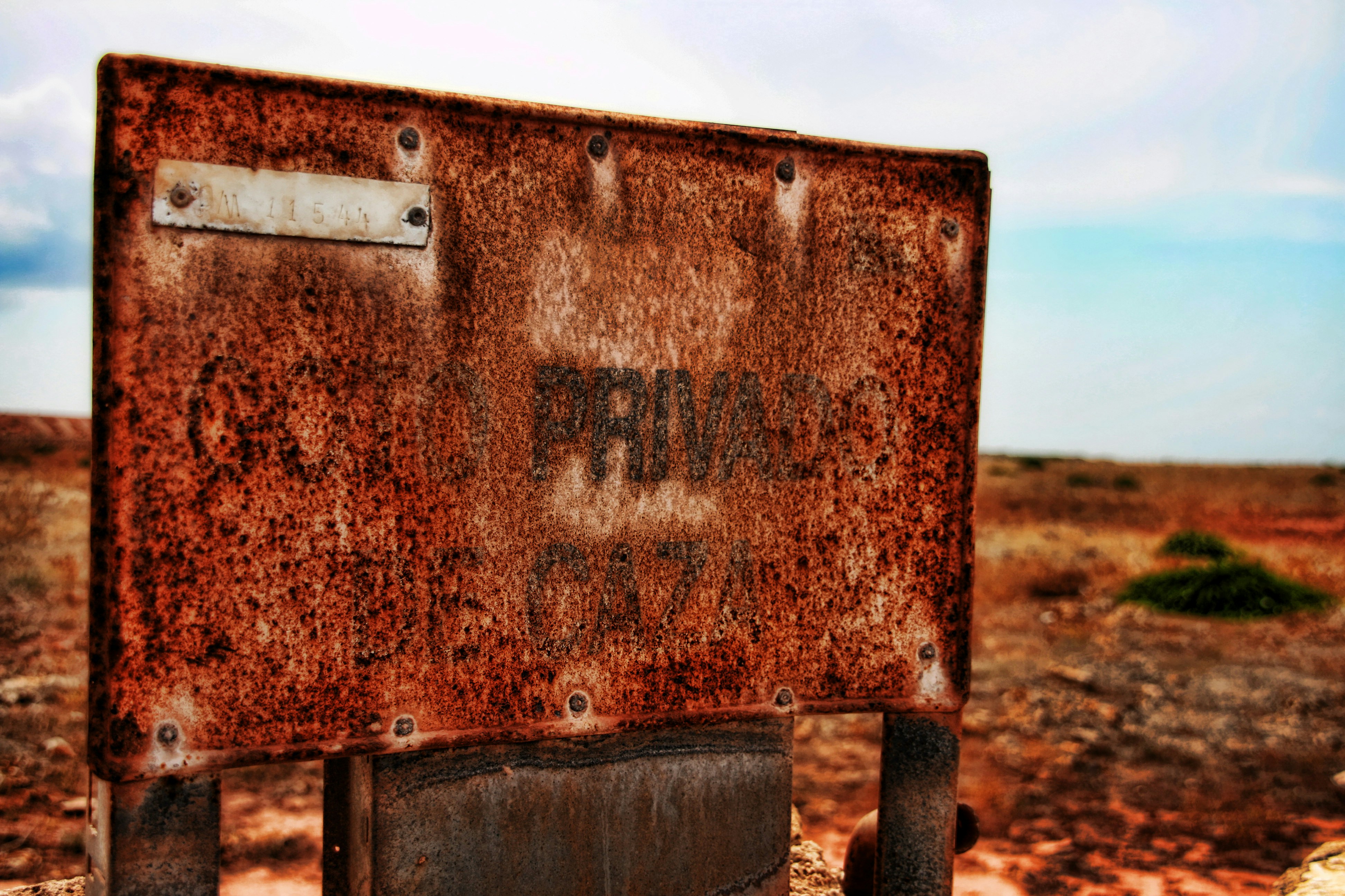 Rusty metal sign in a dry, arid landscape.