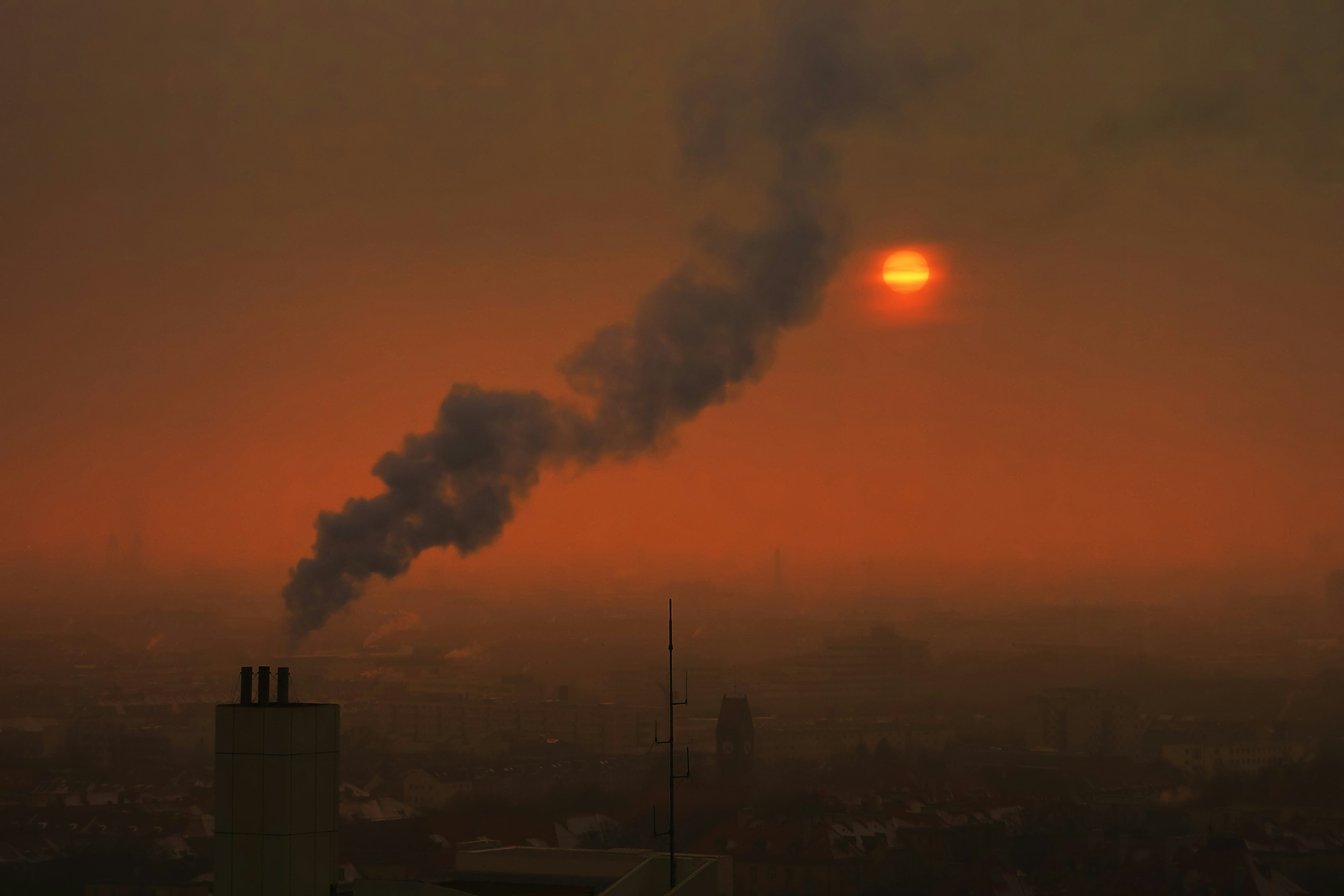 Smoke billows from a chimney against a hazy sunset