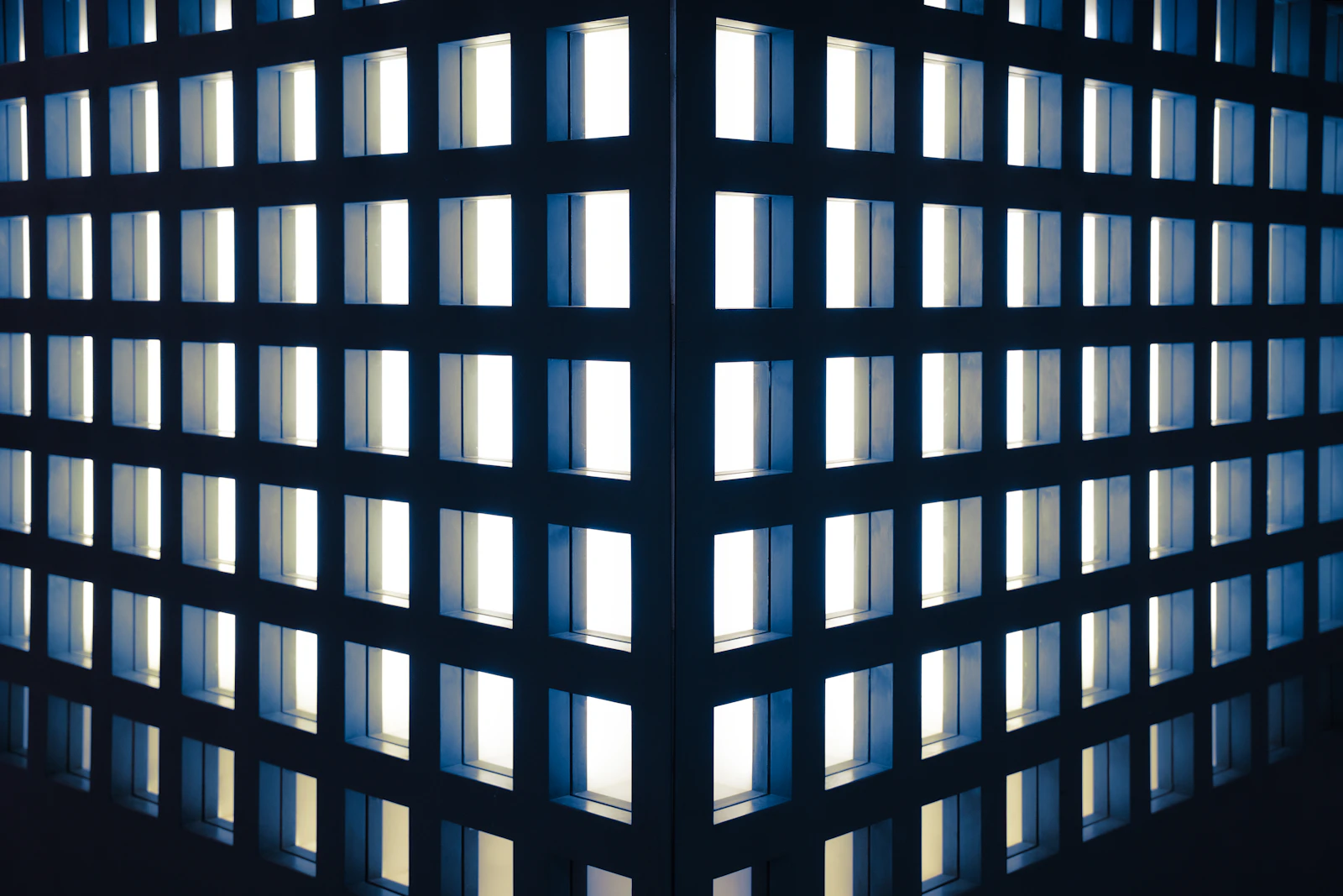 Geometric grid of warmly illuminated square windows on a dark building facade at night