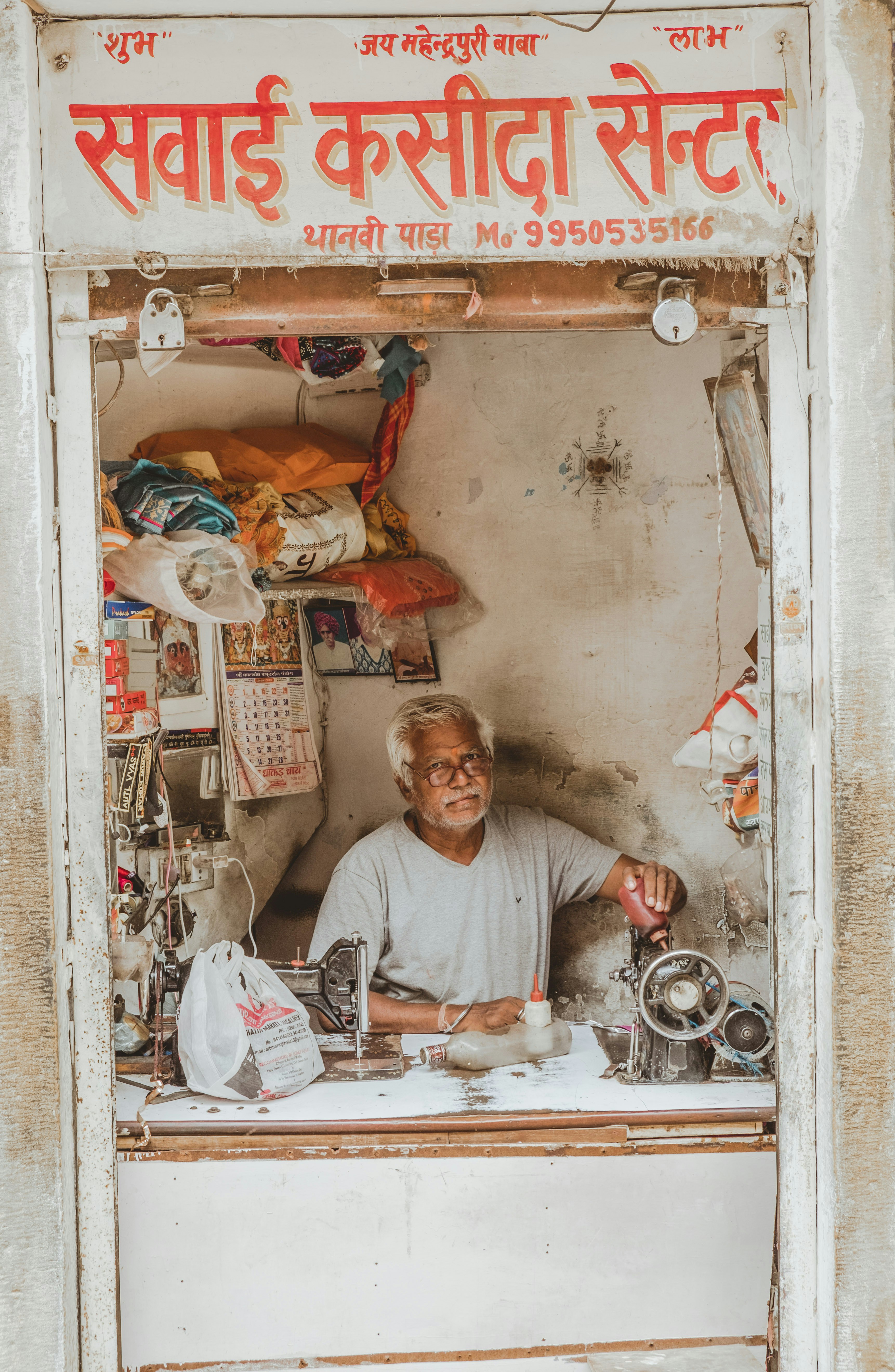 An elderly man sewing in a small shop.
