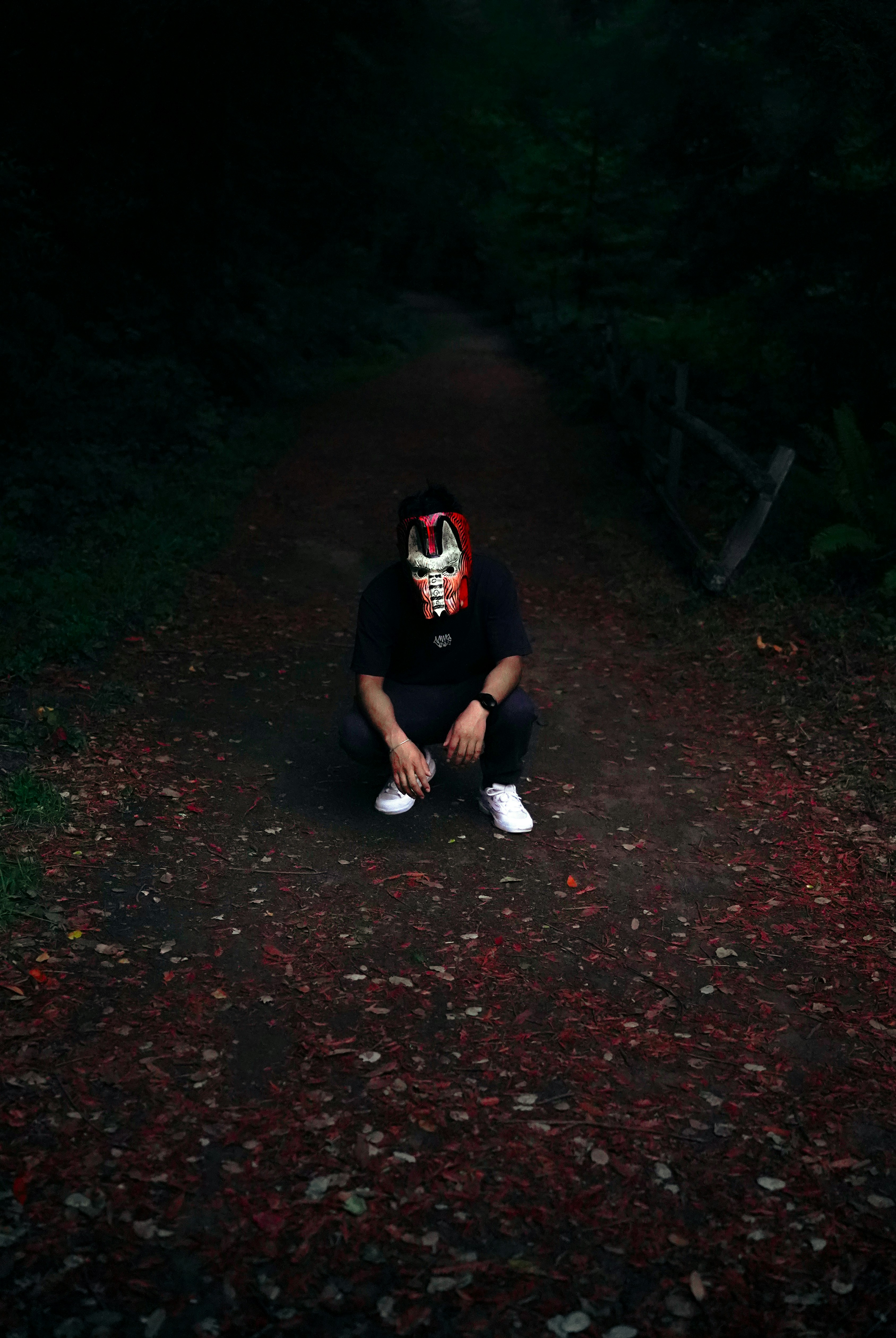 Person in mask crouches on forest path
