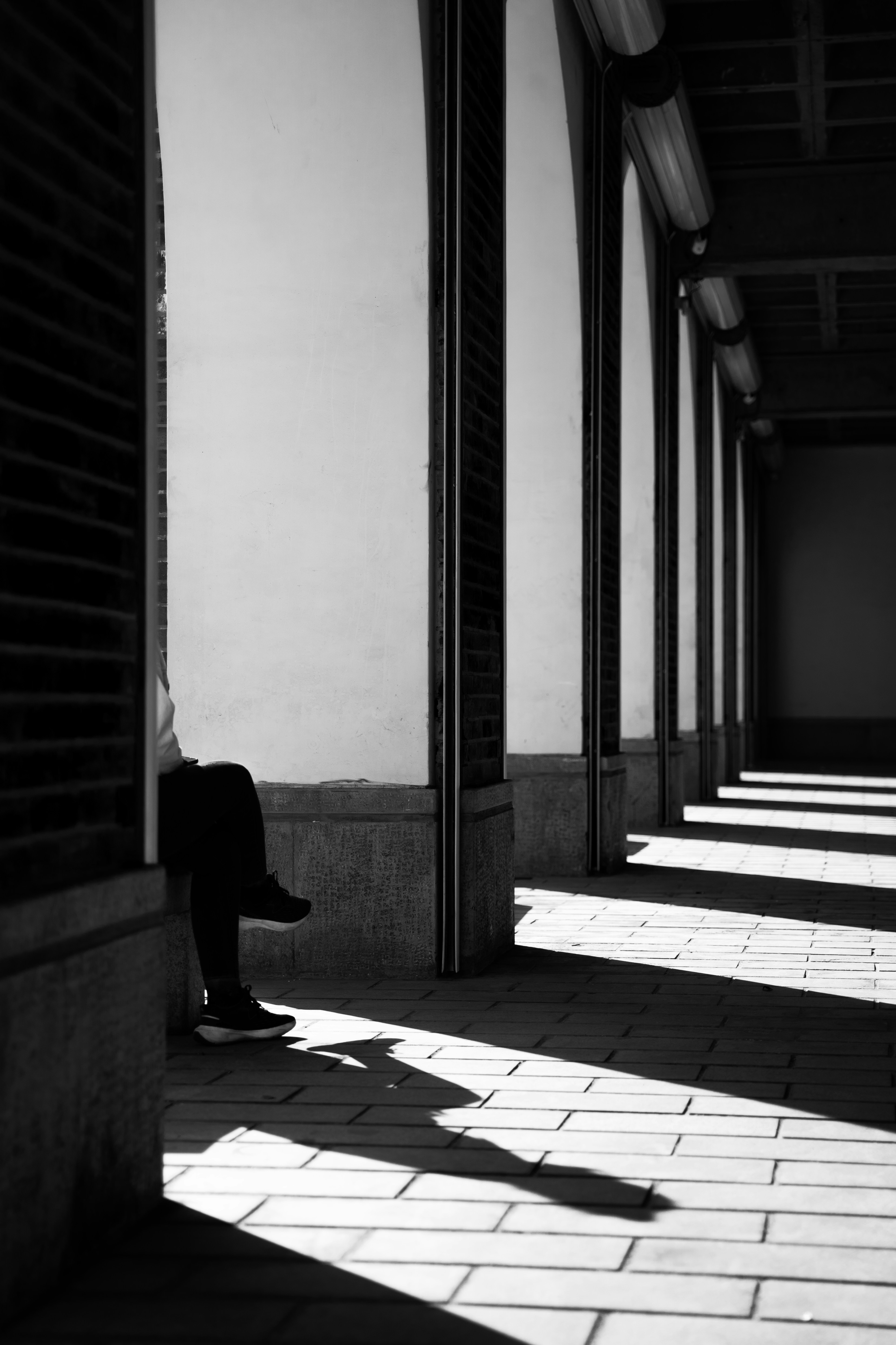 Person sitting in a sunlit hallway with shadows.