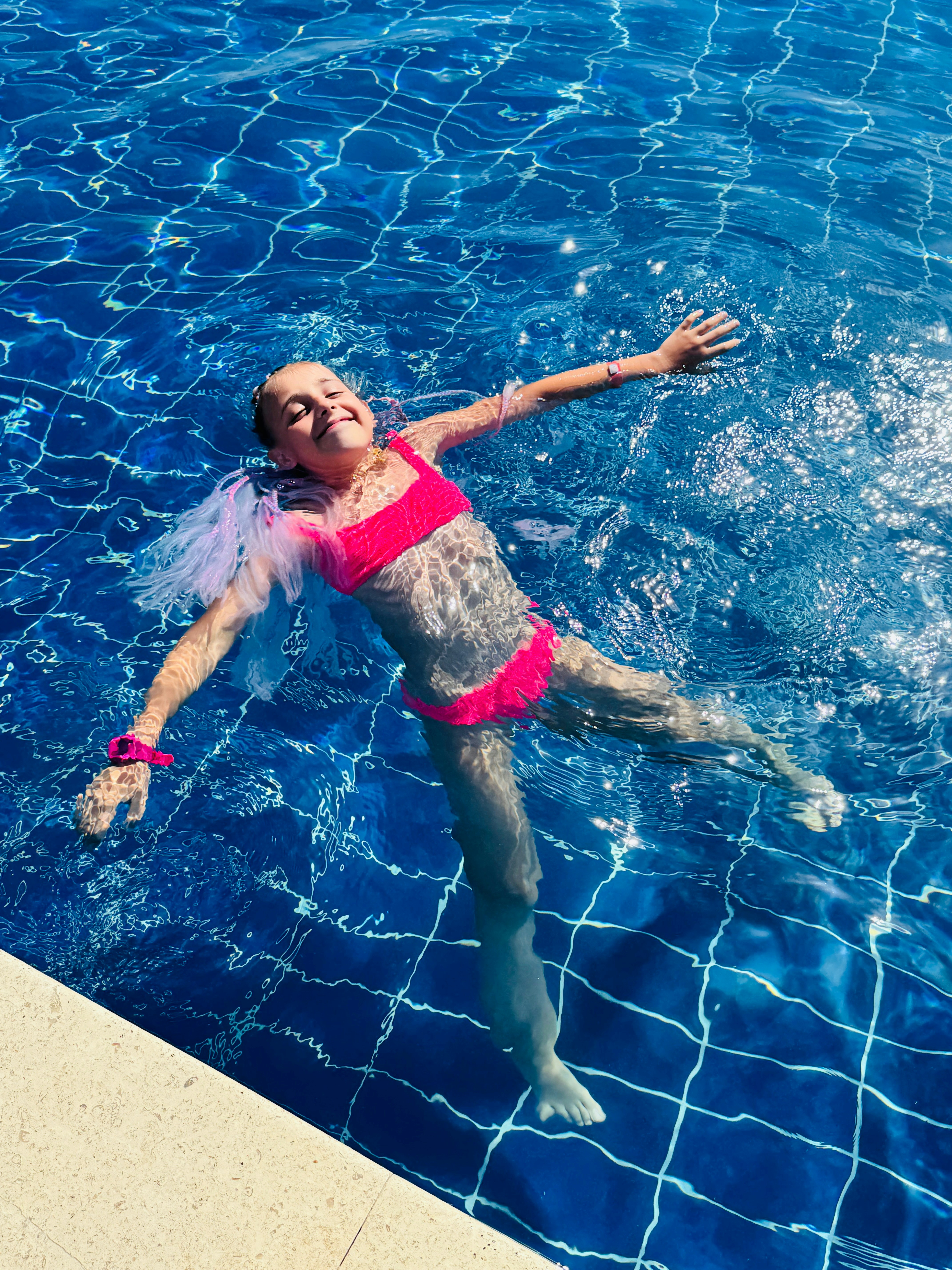 A happy girl floats on her back in a pool.