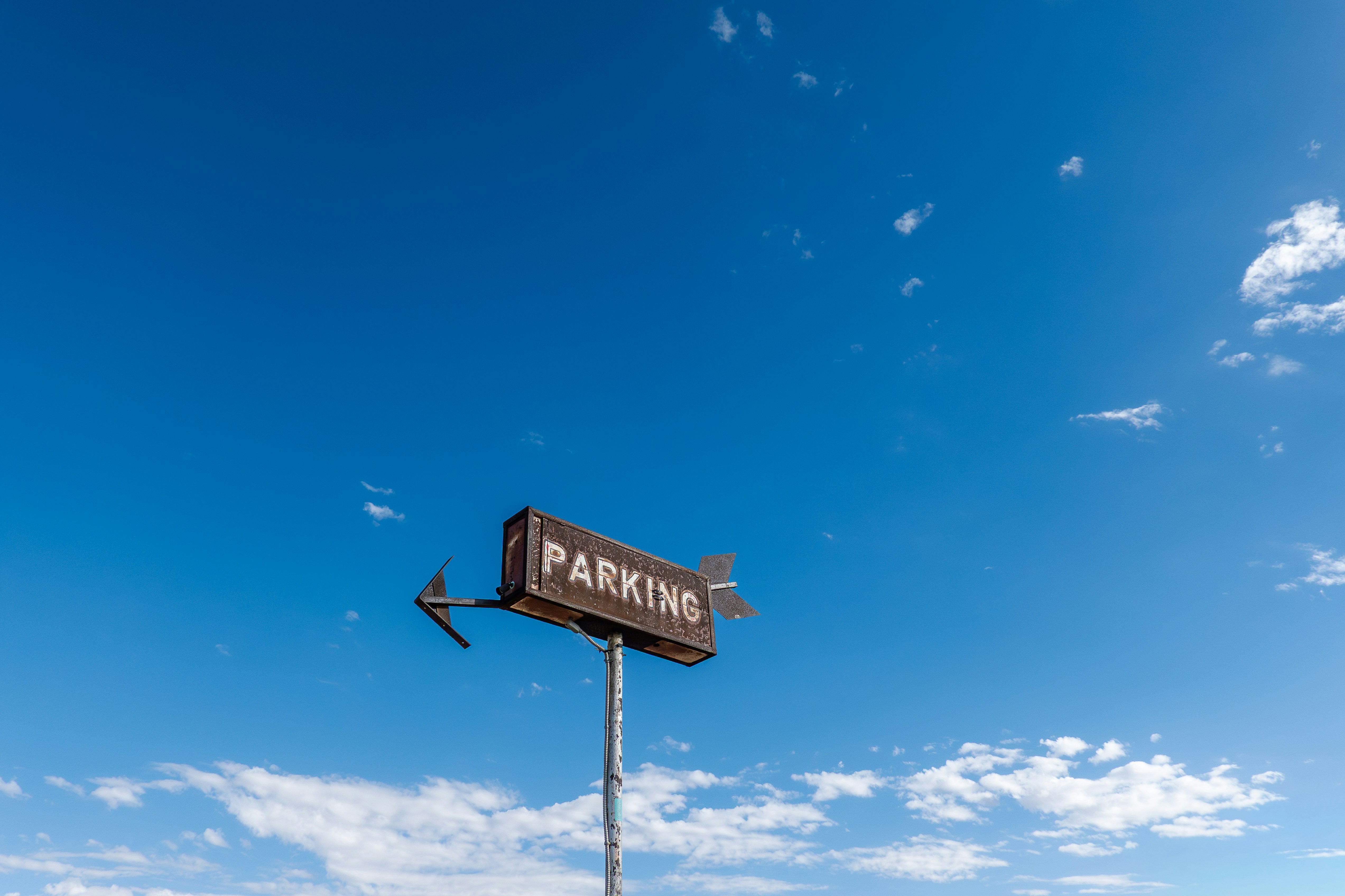 A weathered parking sign against a bright blue sky.