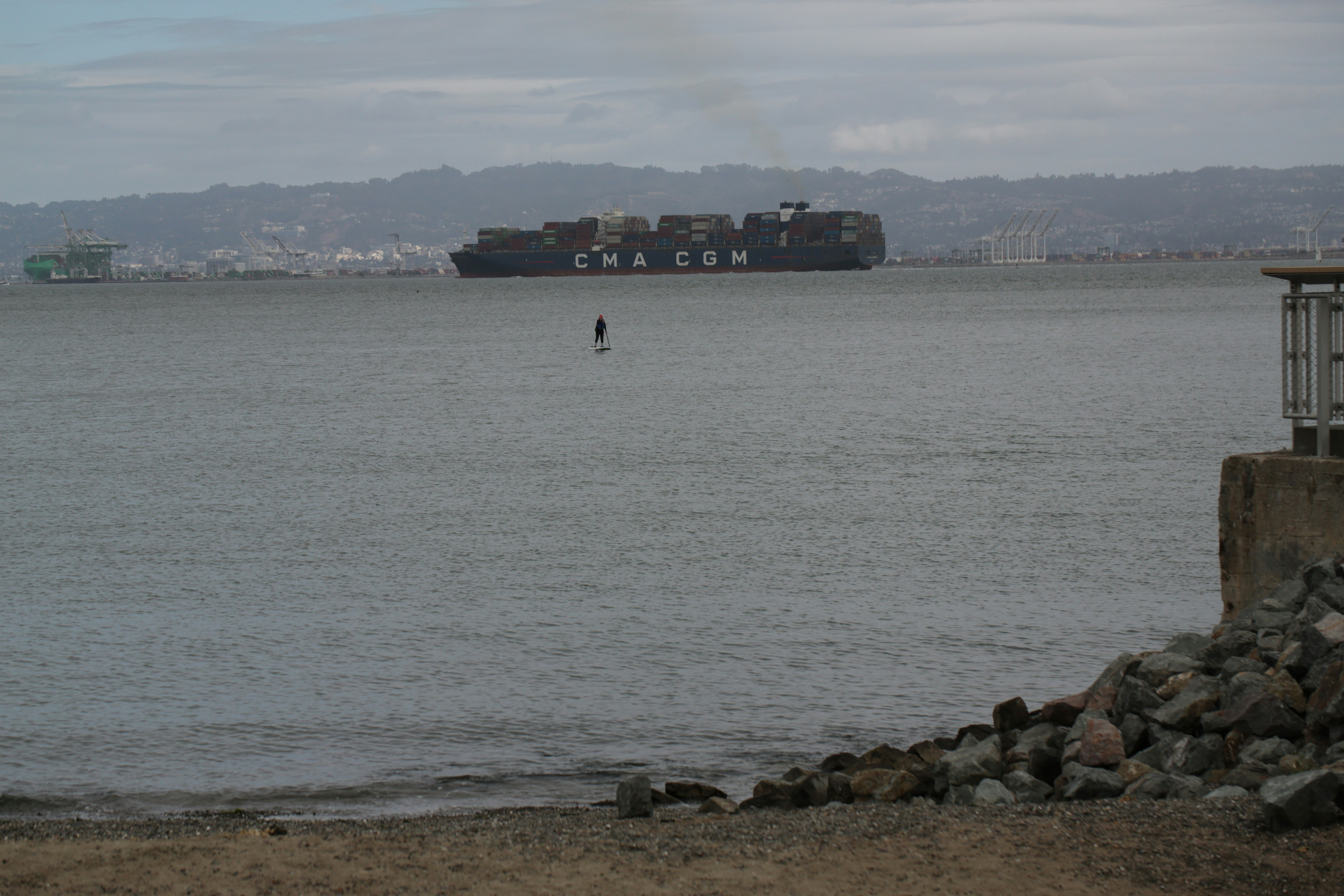 Large cargo ship on the water with a person paddleboarding.