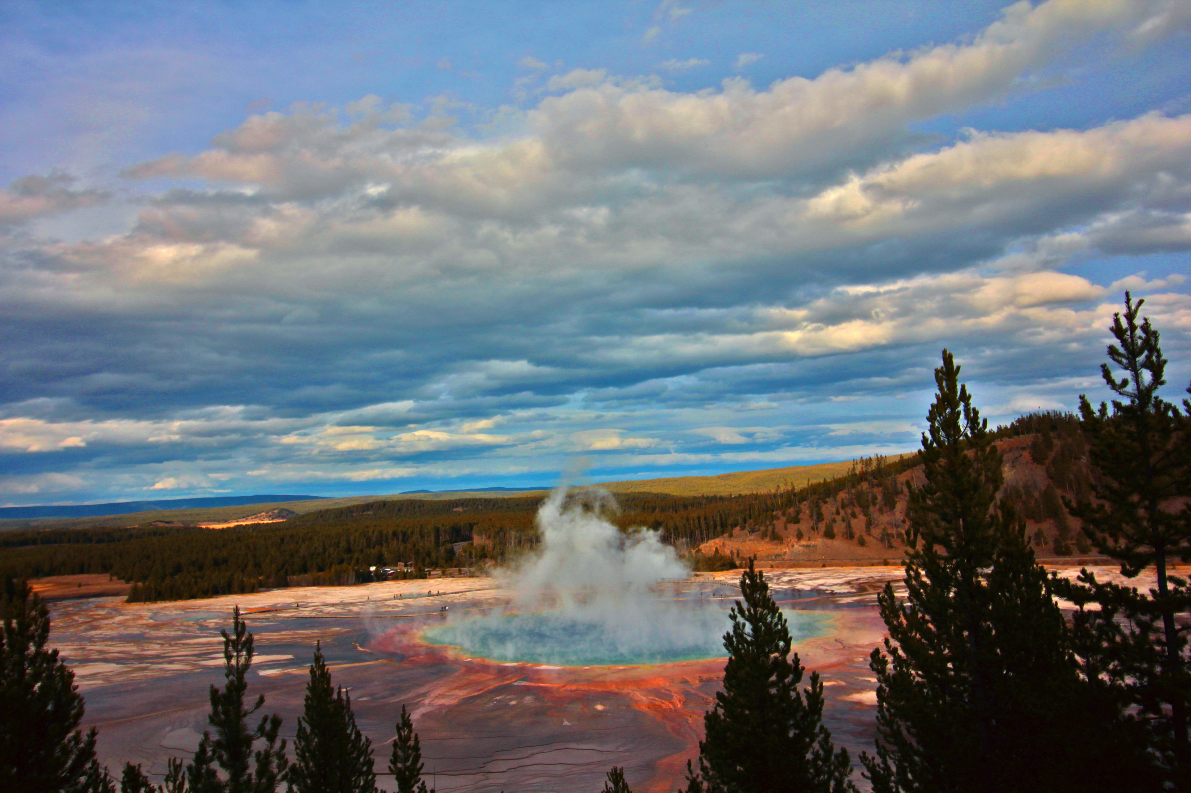Grand prismatic spring erupting steam under cloudy sky.