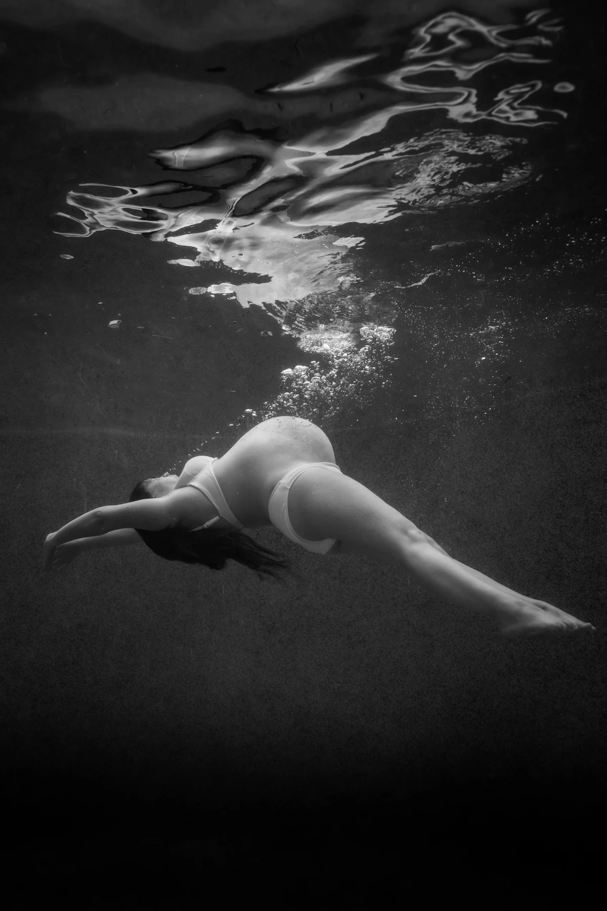 Pregnant woman swimming gracefully underwater in black and white