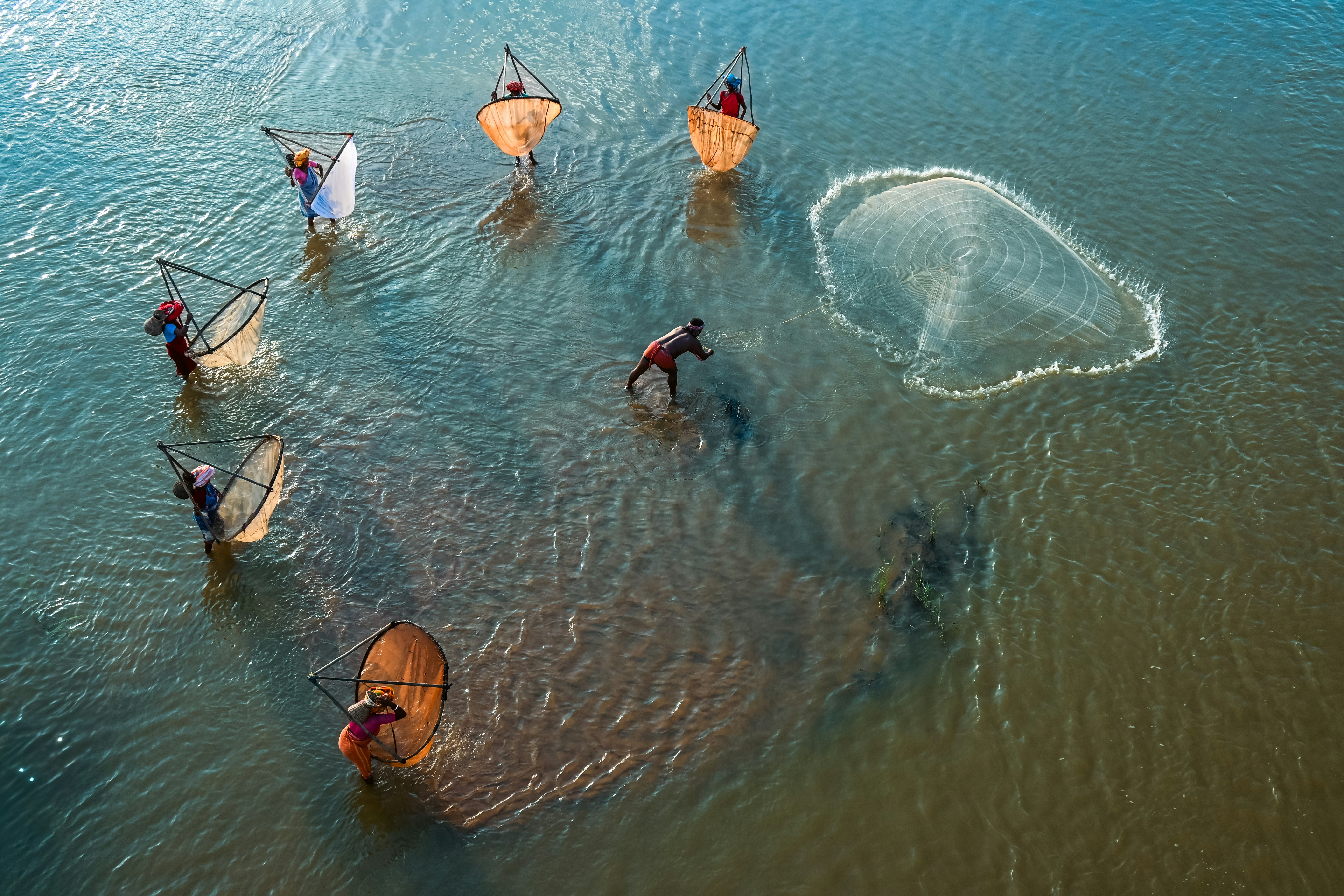 Fishermen casting nets in a body of water.