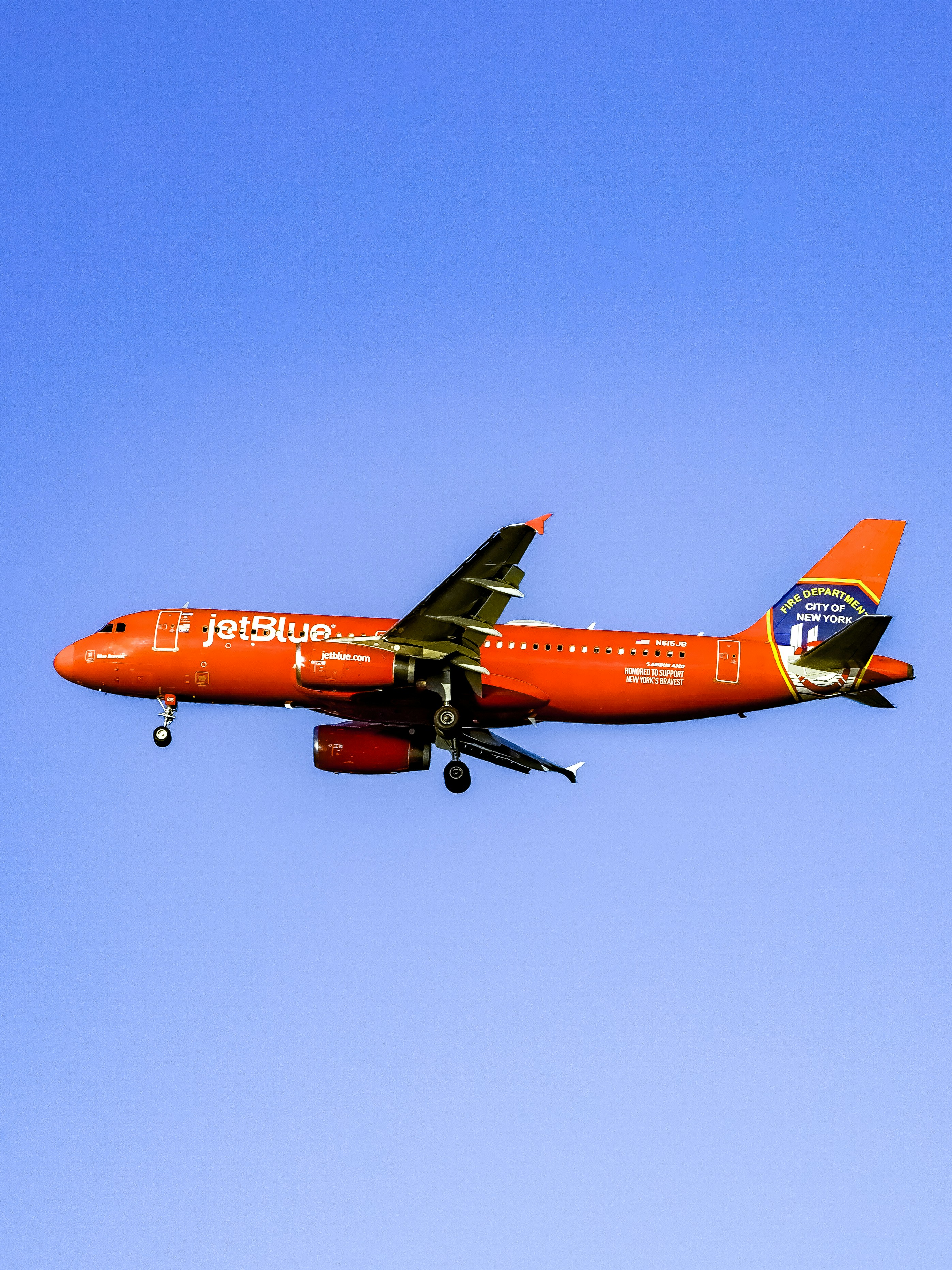 Ein orangefarbenes Flugzeug, das in strahlend blauem Himmel fliegt.