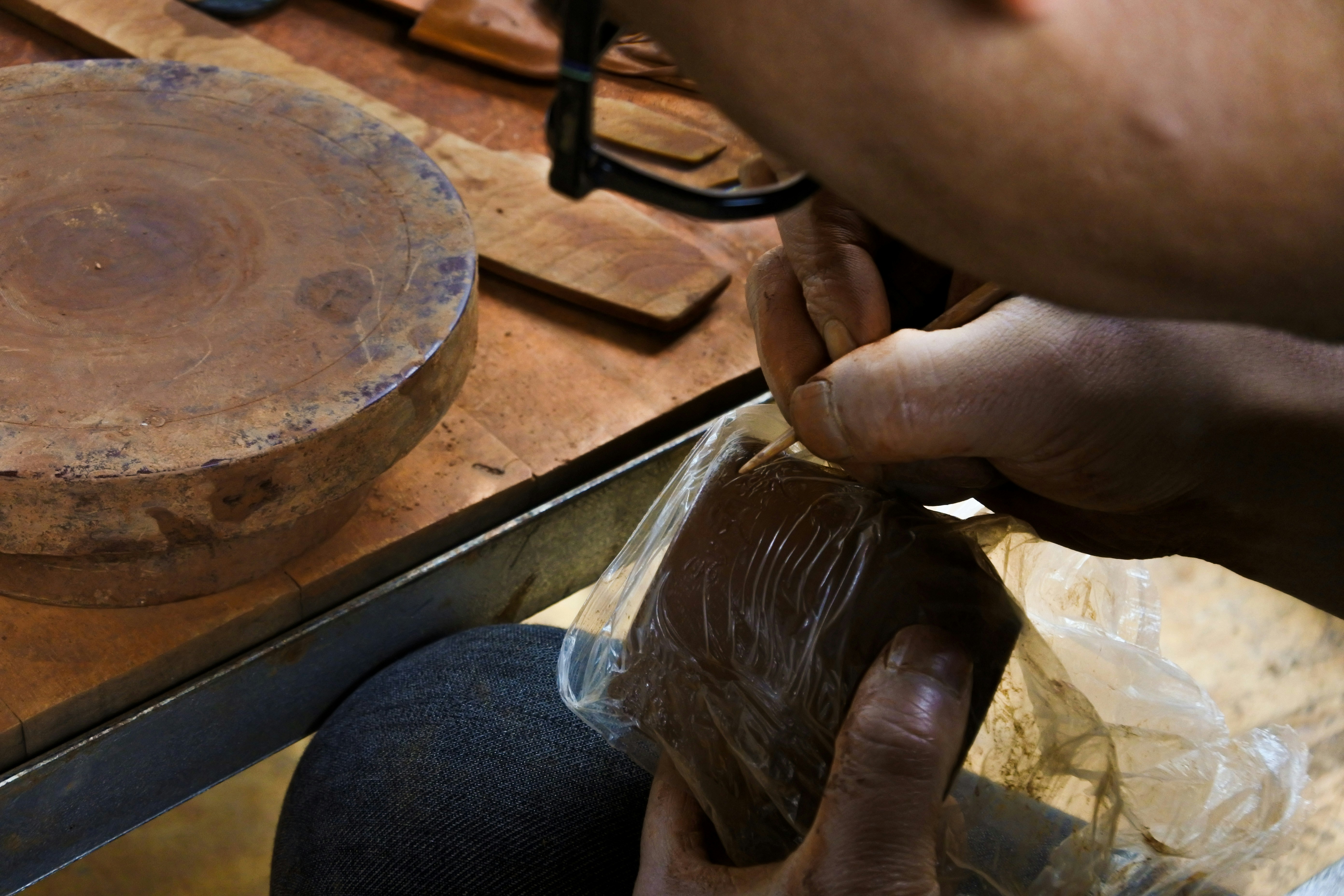 Hands carving a wooden object with a tool.