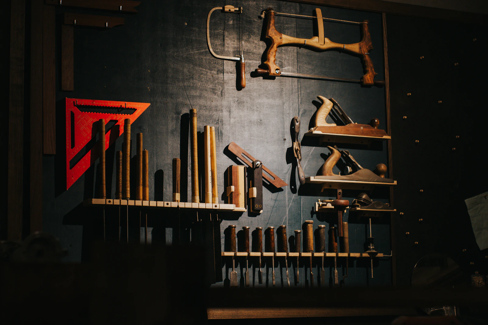 Hand planes, chisels, and saws hung on a workshop wall in warm light