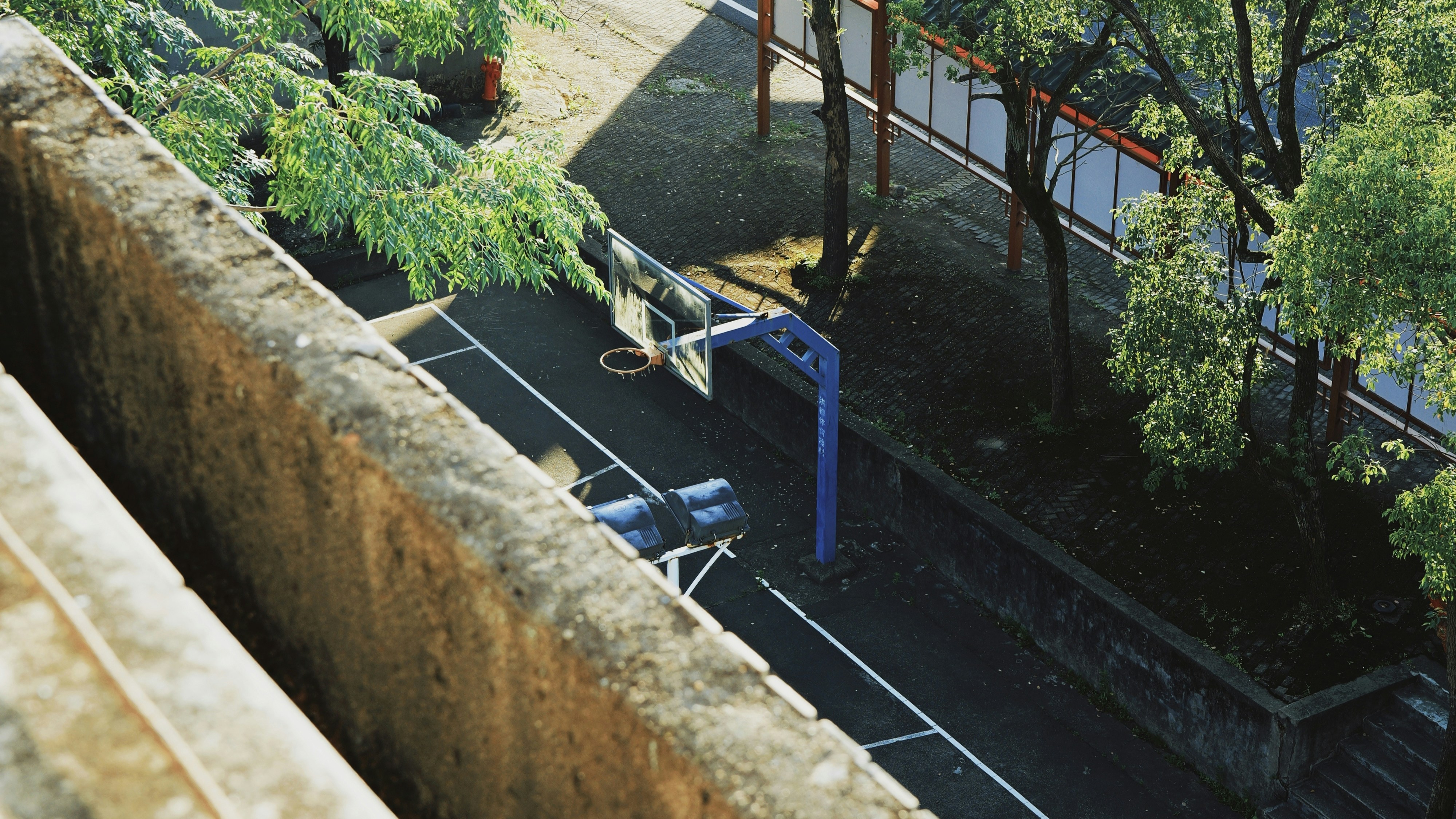 Empty outdoor basketball court with trees and fence