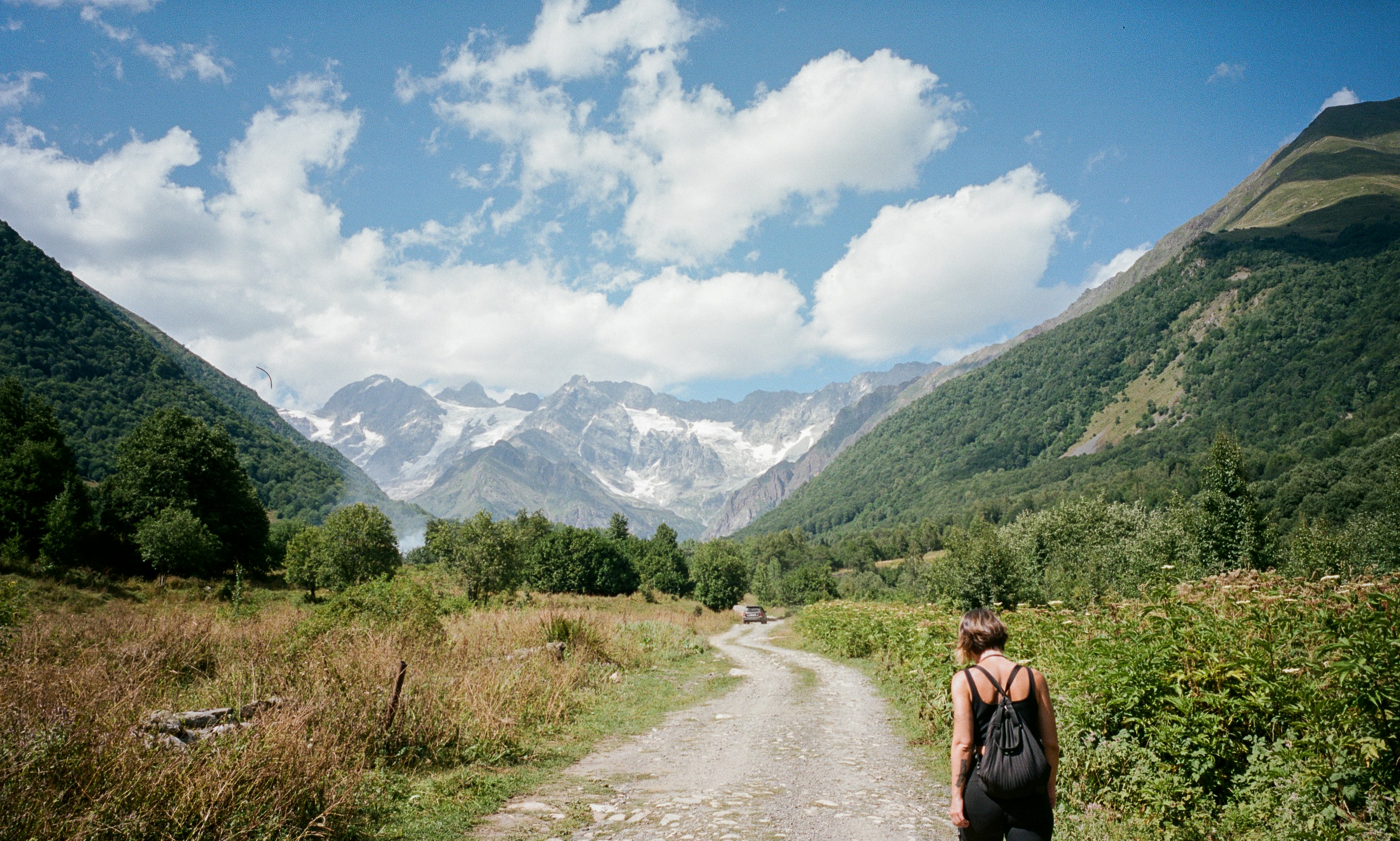 Woman walks on a path towards majestic mountains.