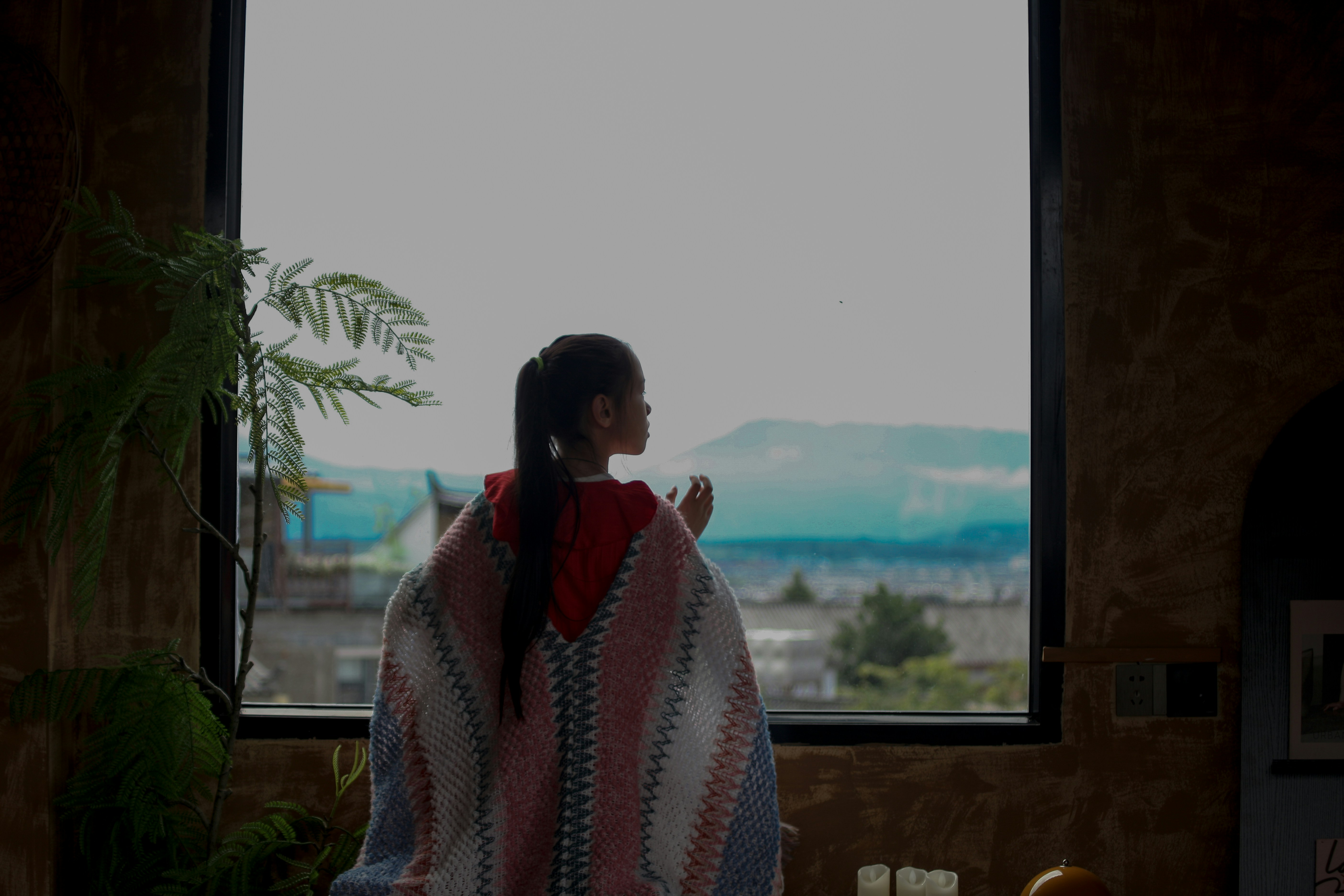 Woman in poncho looking out large window at landscape