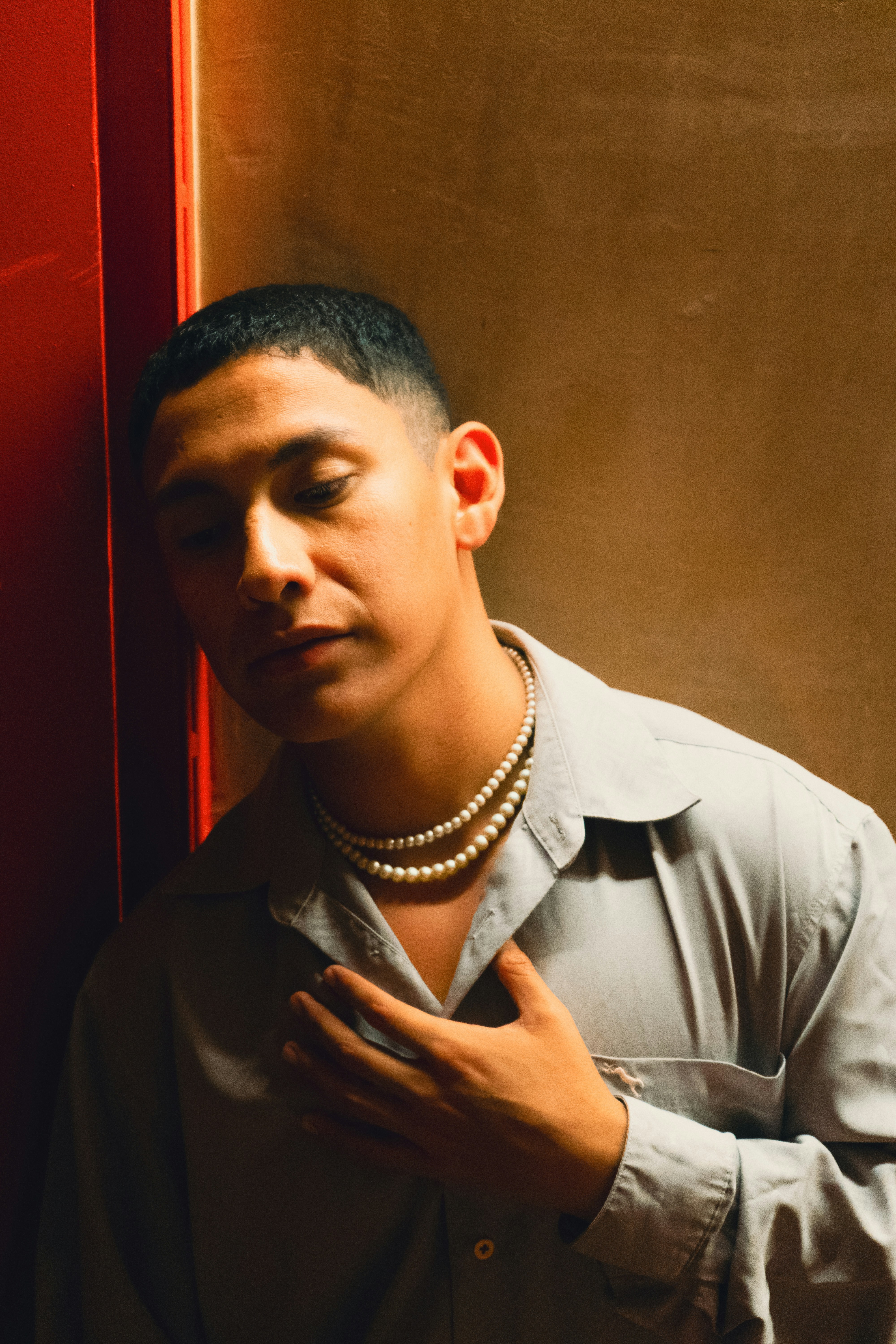 A young man wearing a pearl necklace and collared shirt.