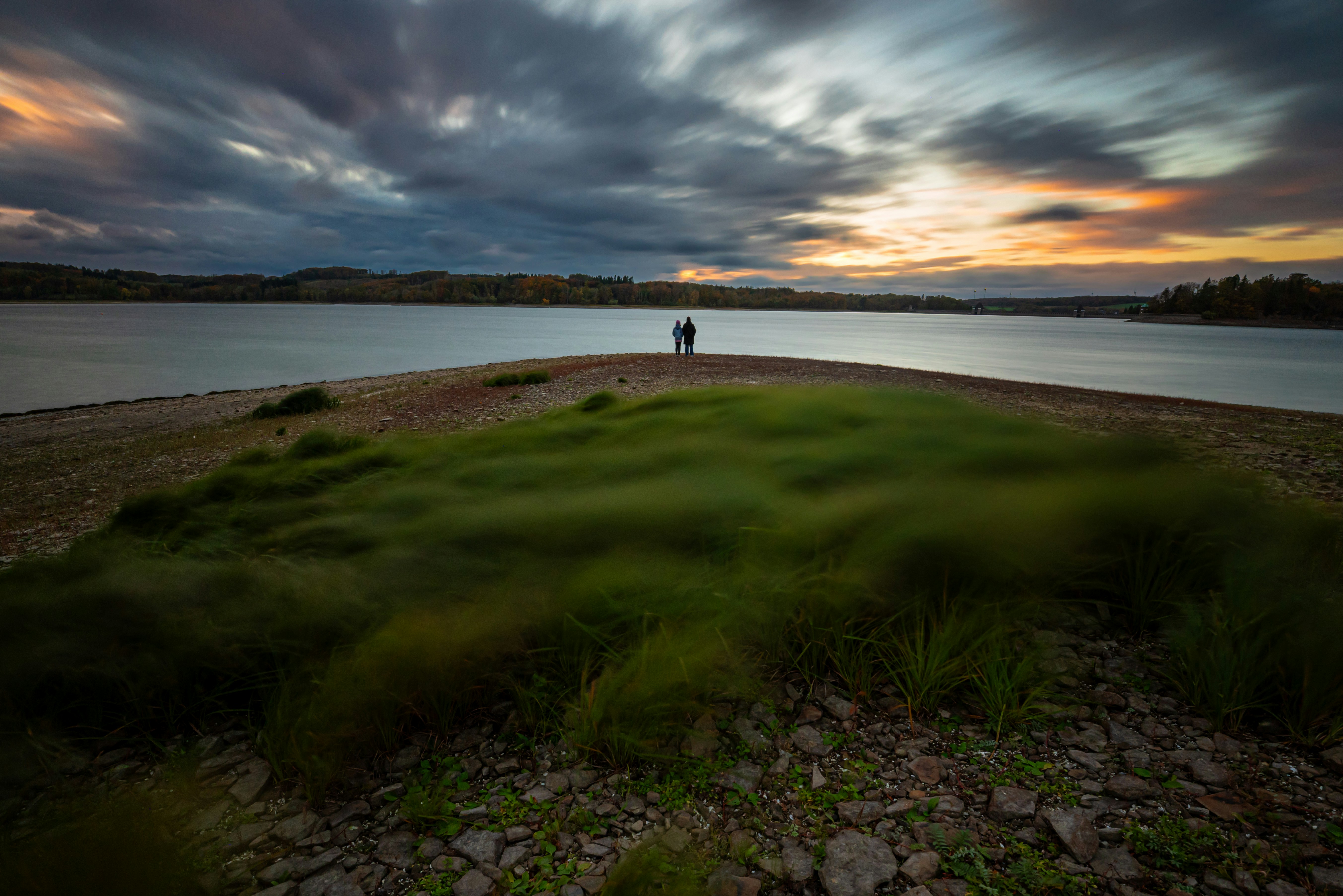 Two people stand on a peninsula at sunset.