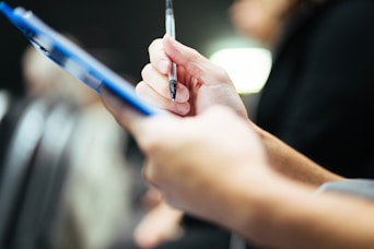 Hand holding pen over a blue clipboard.
