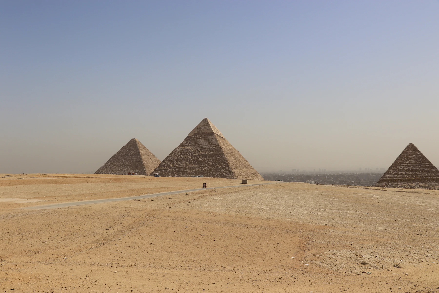 Three pyramids stand in the desert with the Cairo skyline beyond.