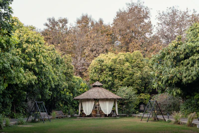 Thatched gazebo with curtains in a lush garden.
