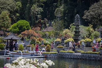 People explore a lush garden with a pond and boat.
