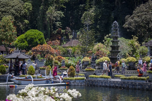 People explore a lush garden with a pond and boat.