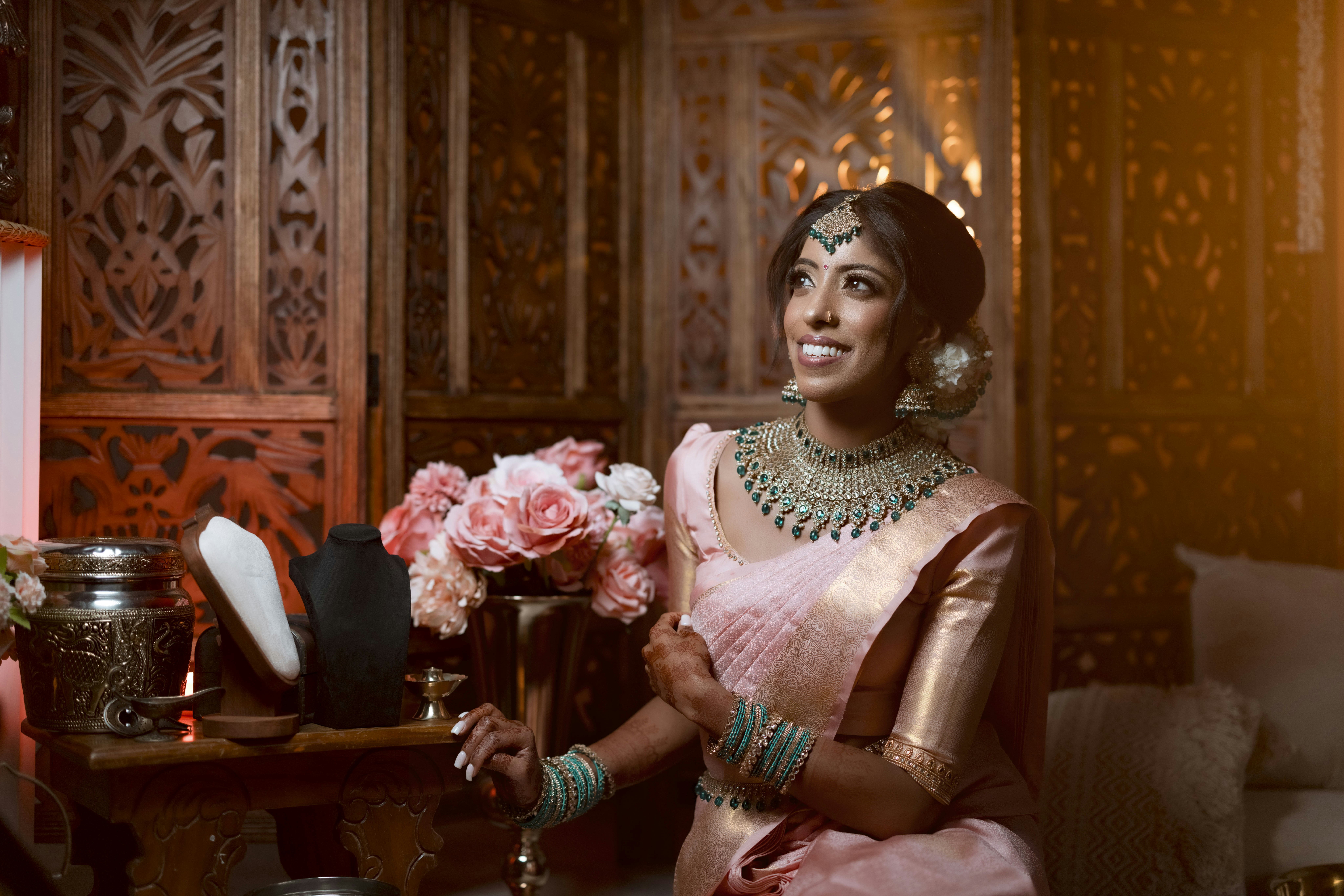 A smiling woman in a pink sari and jewelry.