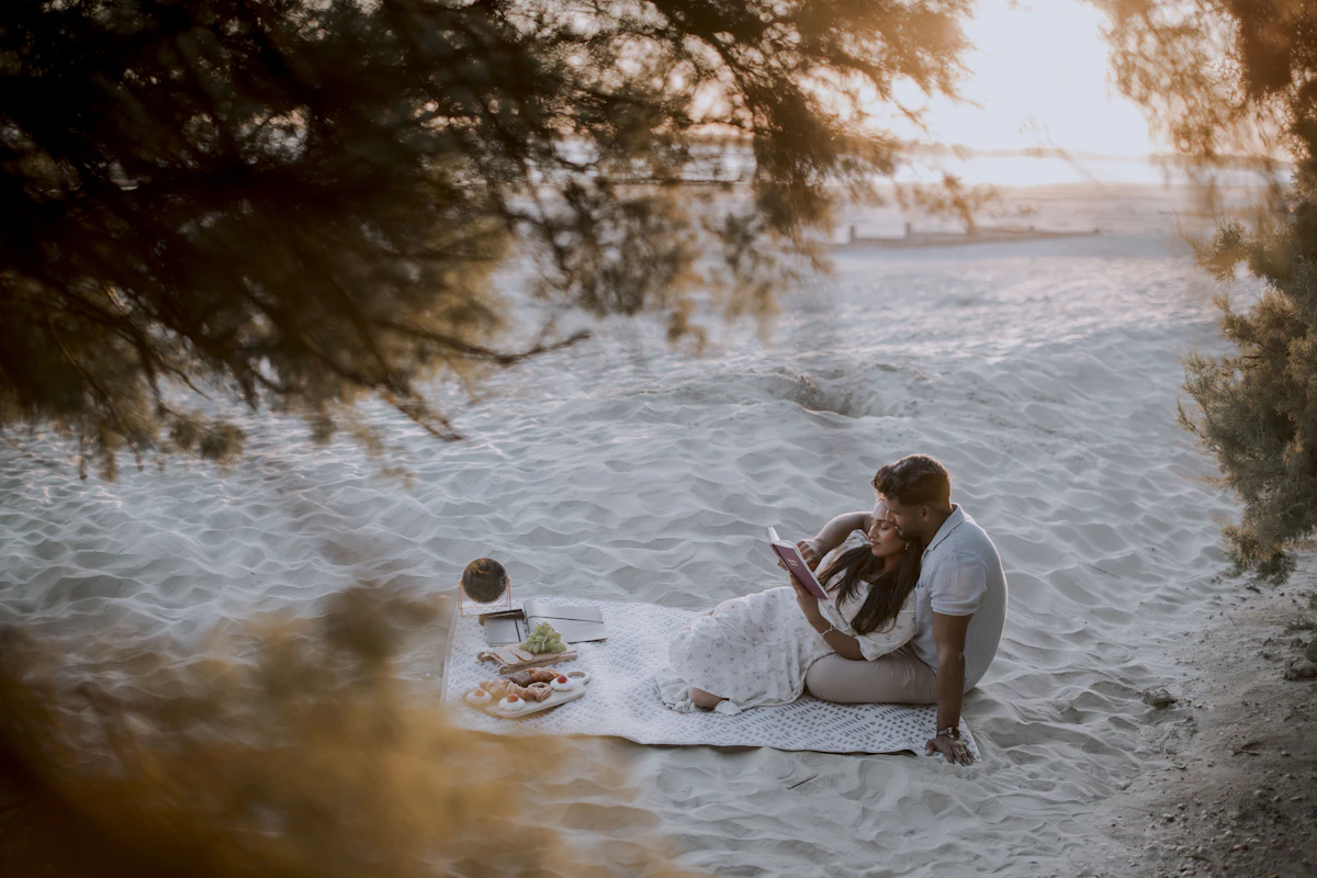 Couple enjoying a romantic picnic date on a sandy beach blanket at sunset