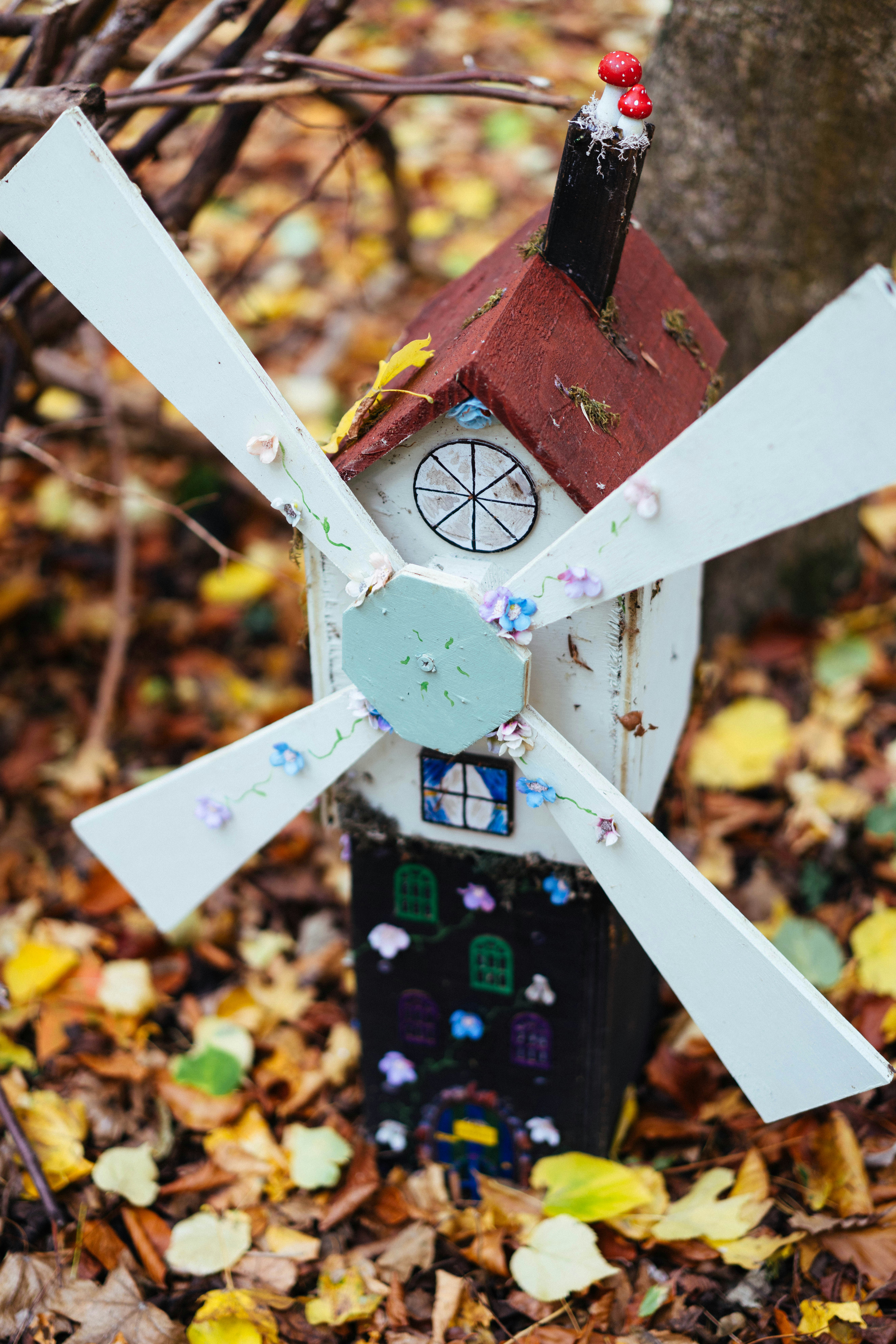 A small, whimsical windmill decoration among autumn leaves.