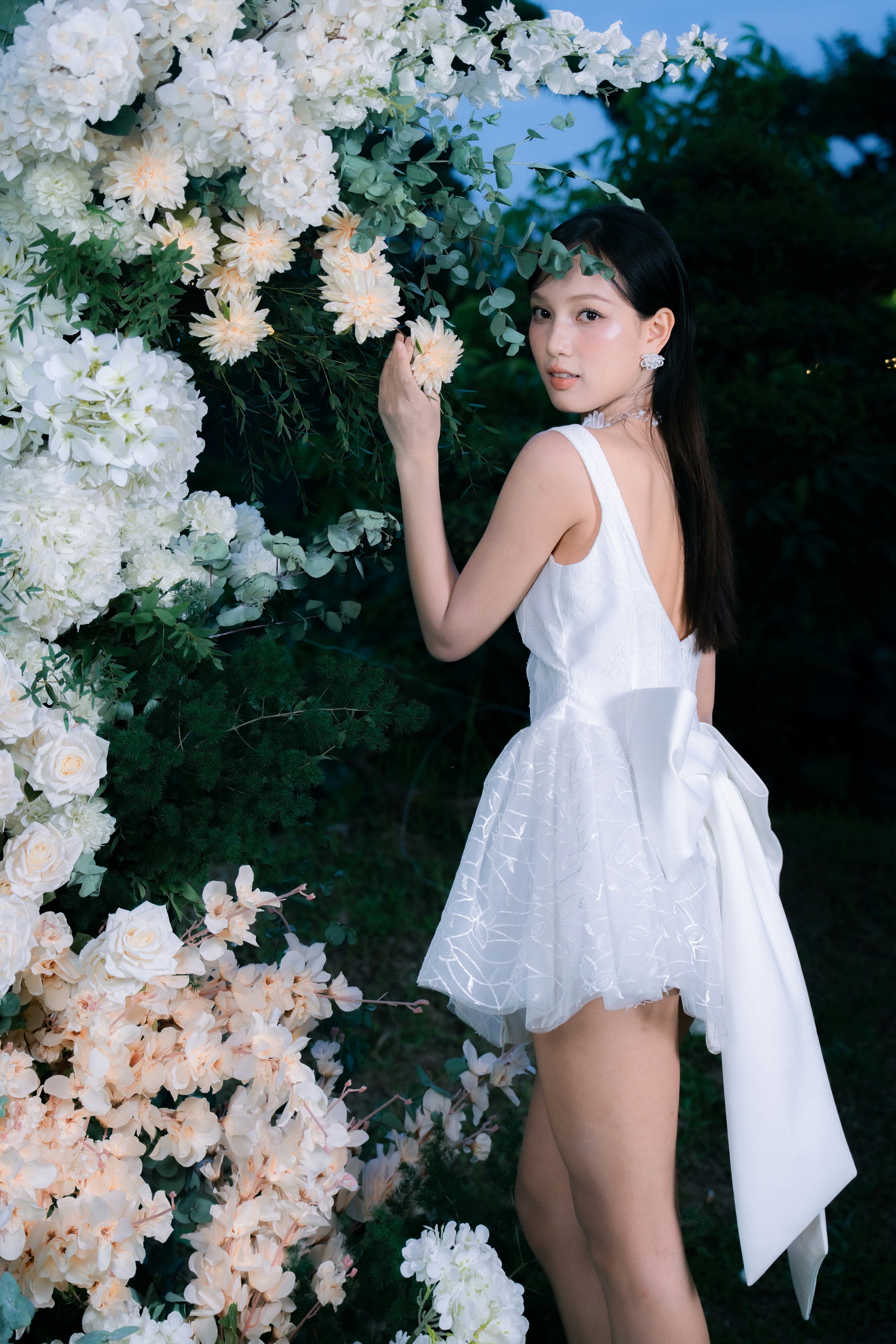 Woman in white dress posing by floral archway