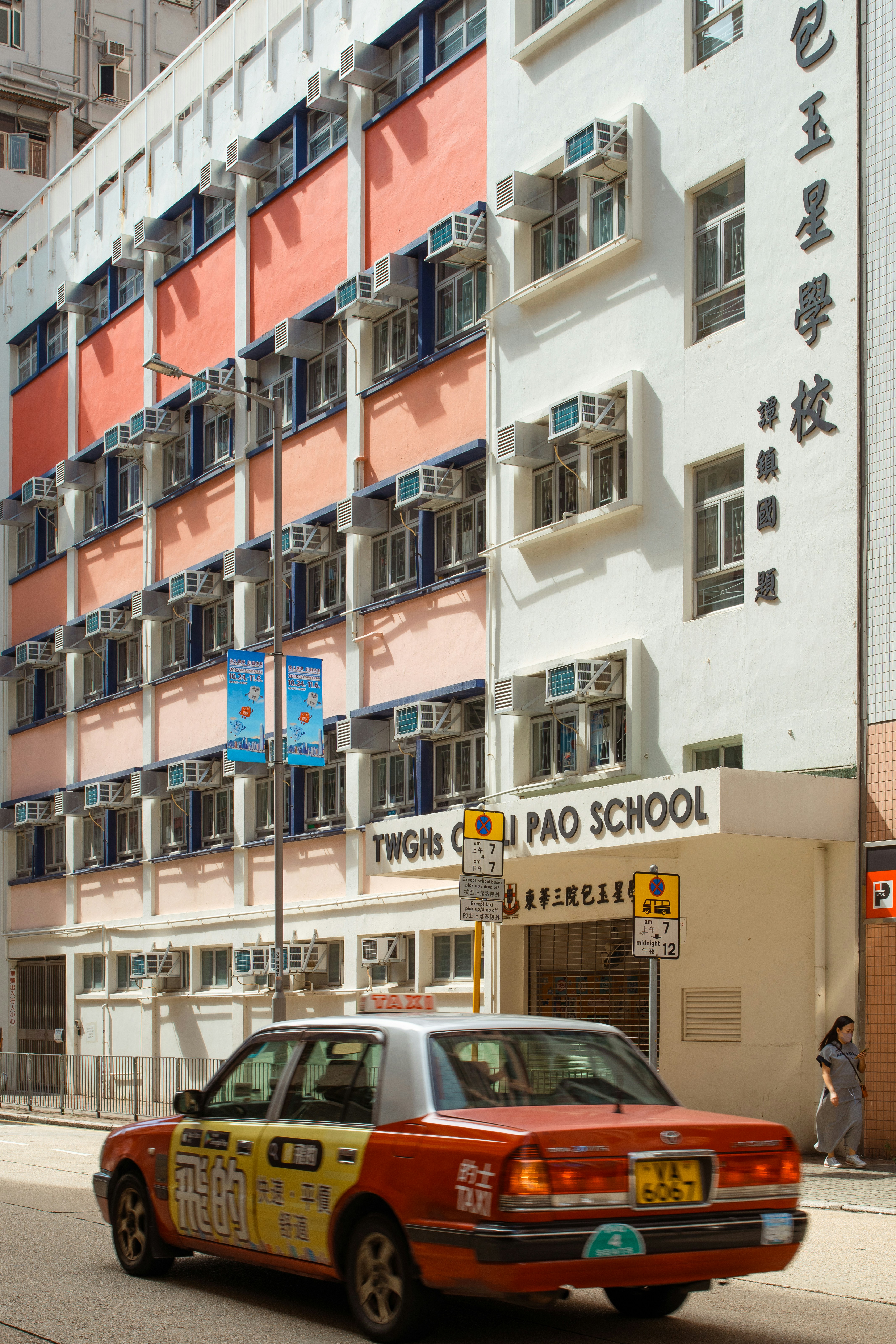 Red taxi drives past a school building in hong kong.