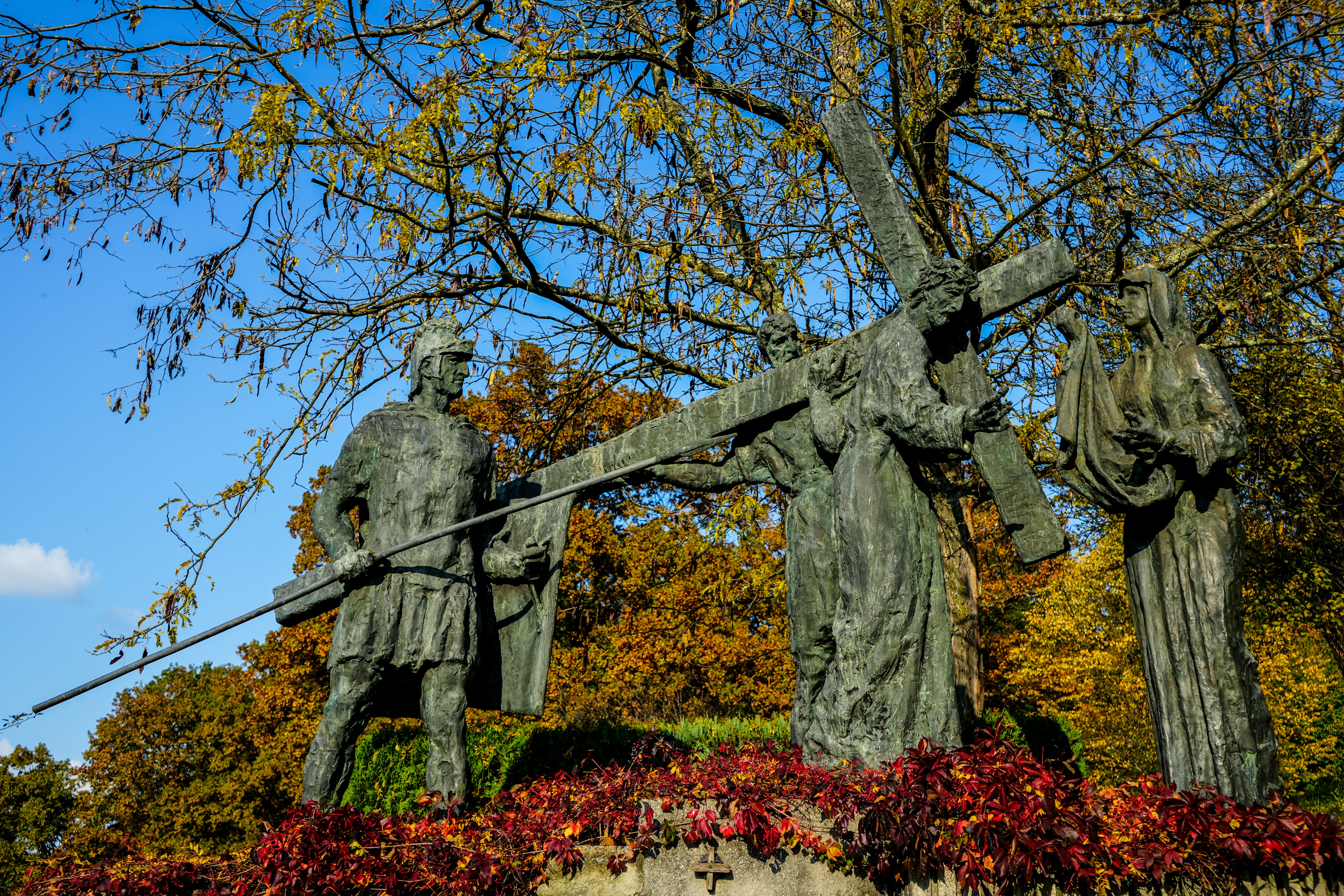 Bronzestatuen stellen Figuren dar, die im Freien ein Kreuz tragen.