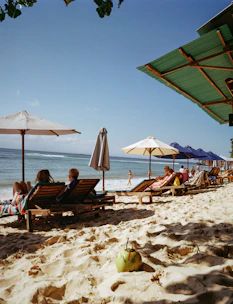 People relax on lounge chairs at a sunny beach.