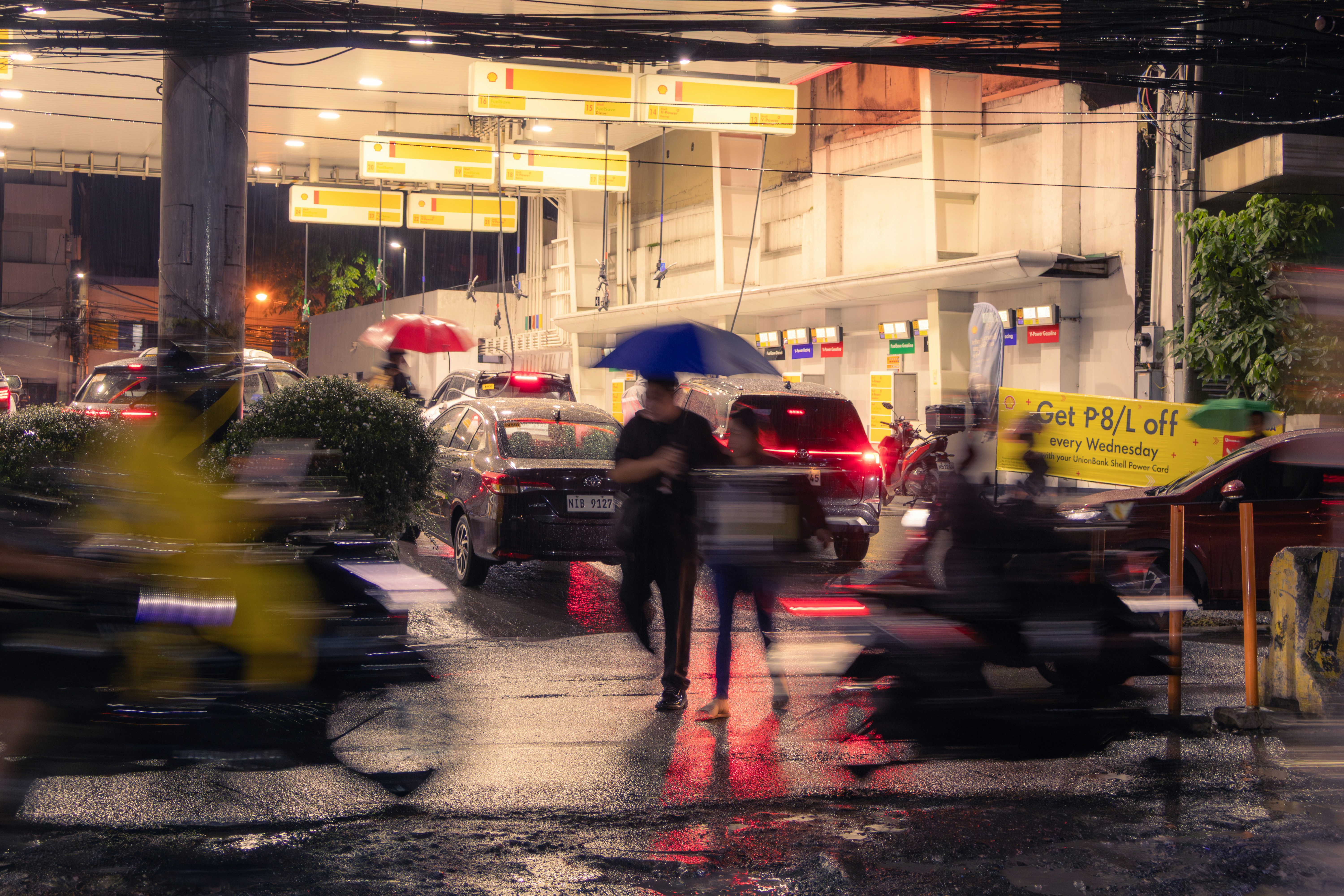 People with umbrellas walk on wet street at night.
