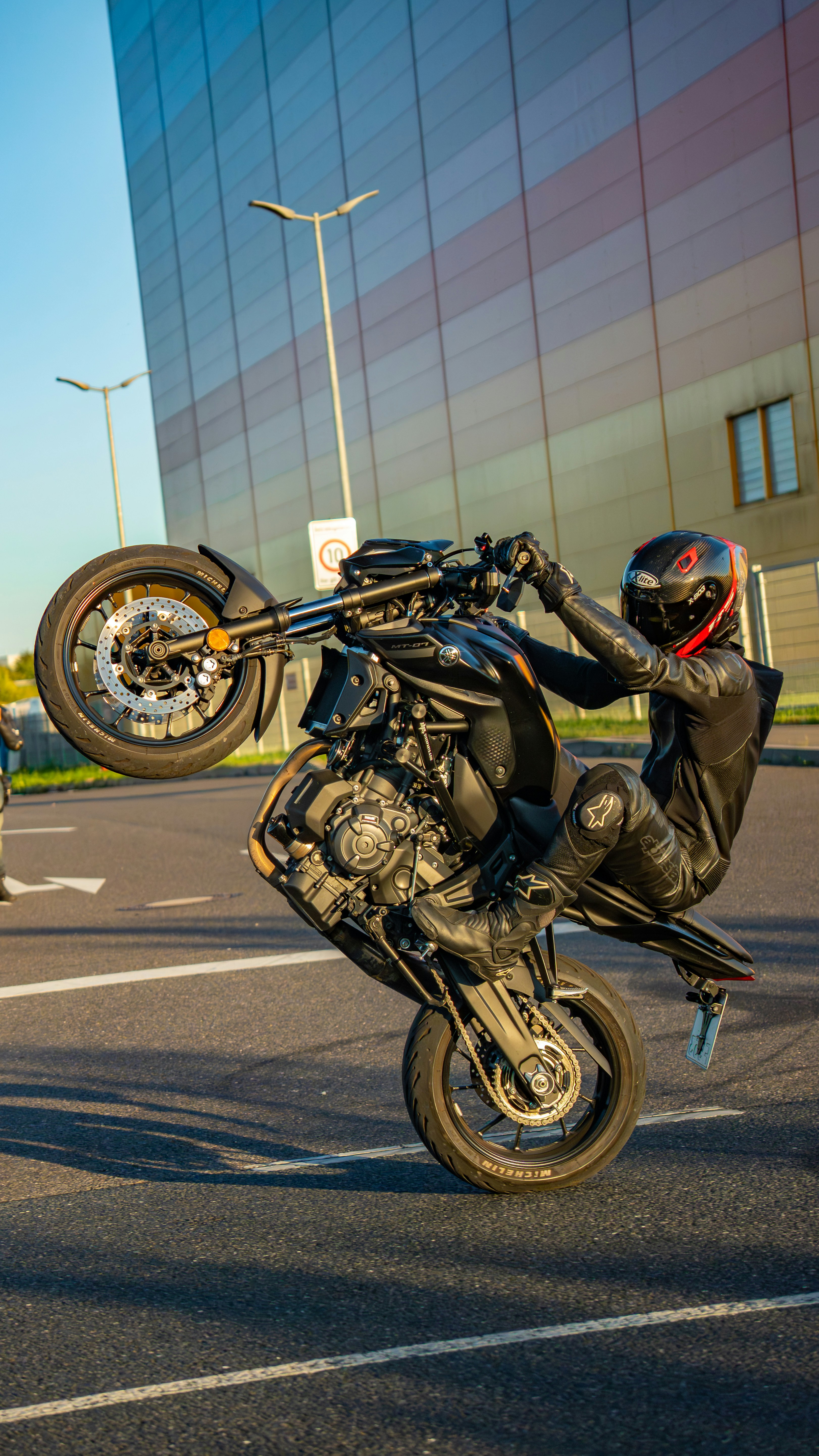 Motorcyclist performs a wheelie in front of a modern building.