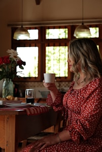 Woman in red dress holding coffee cup at table.