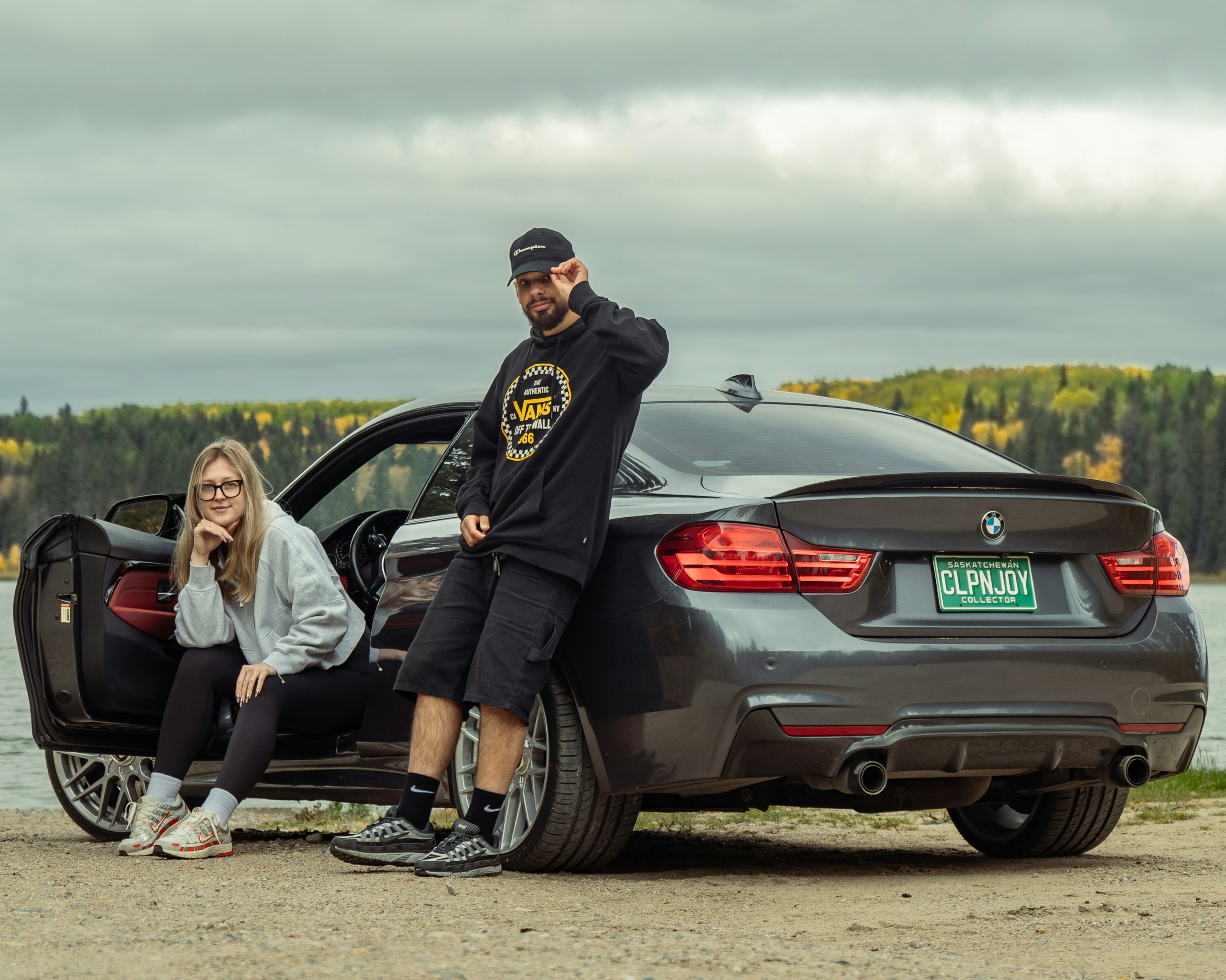 Couple posing by a sleek car near a lake.