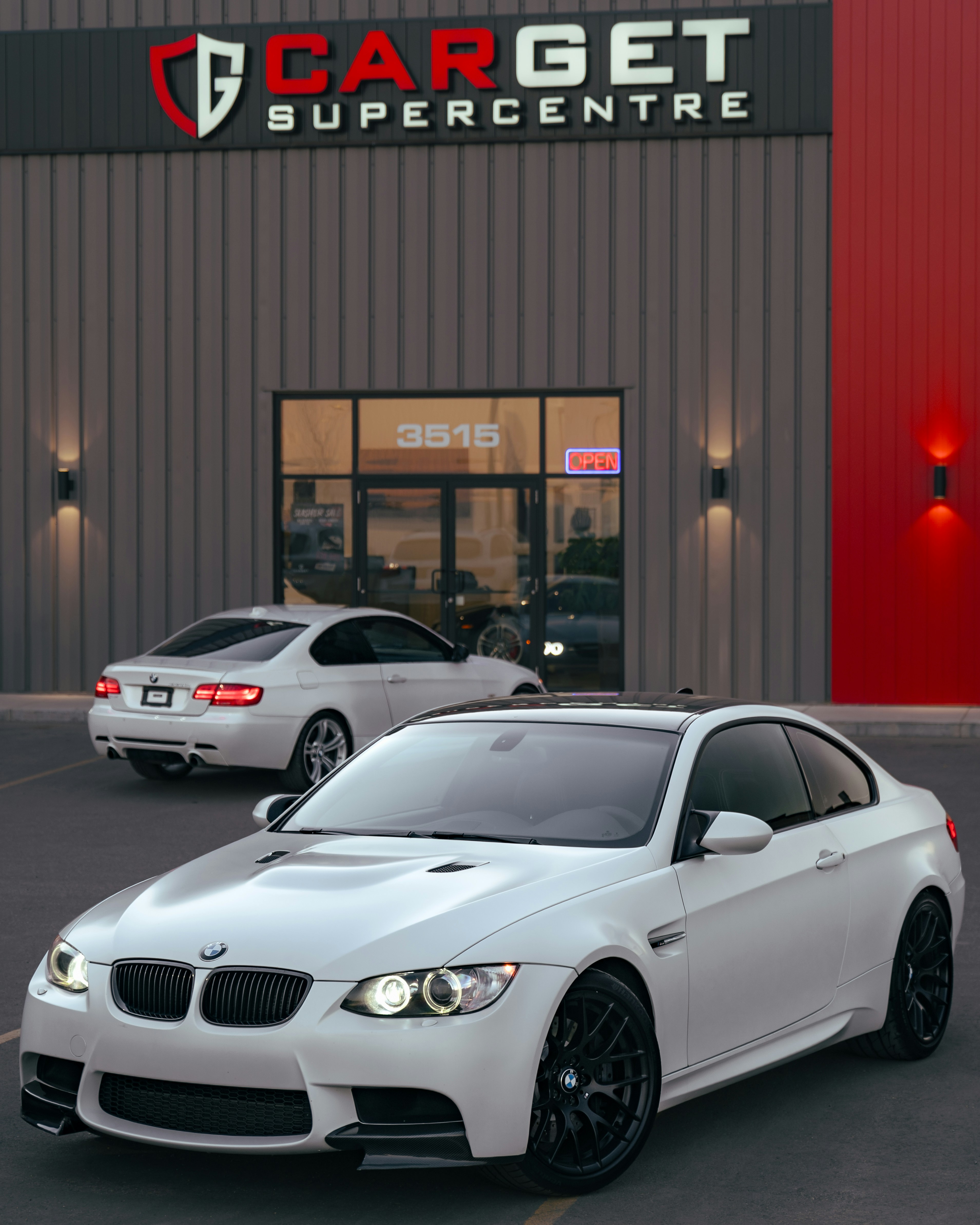 Two white bmws parked outside a dealership.