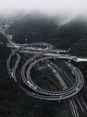 Complex highway interchange surrounded by misty green mountains.