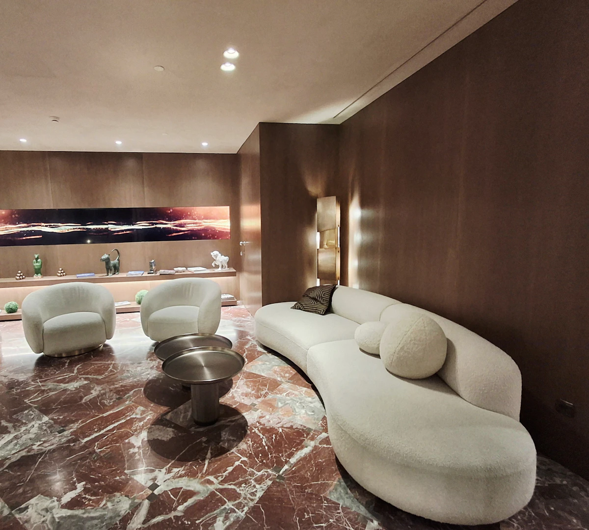 A curved ivory sofa and two round armchairs on a red-veined marble floor