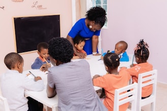 Teacher guiding children drawing at a table.
