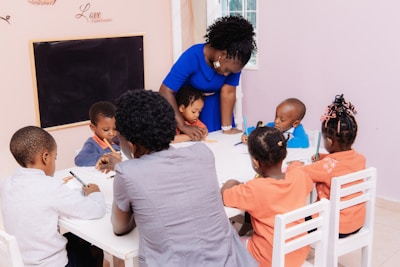 Teacher guiding children drawing at a table.