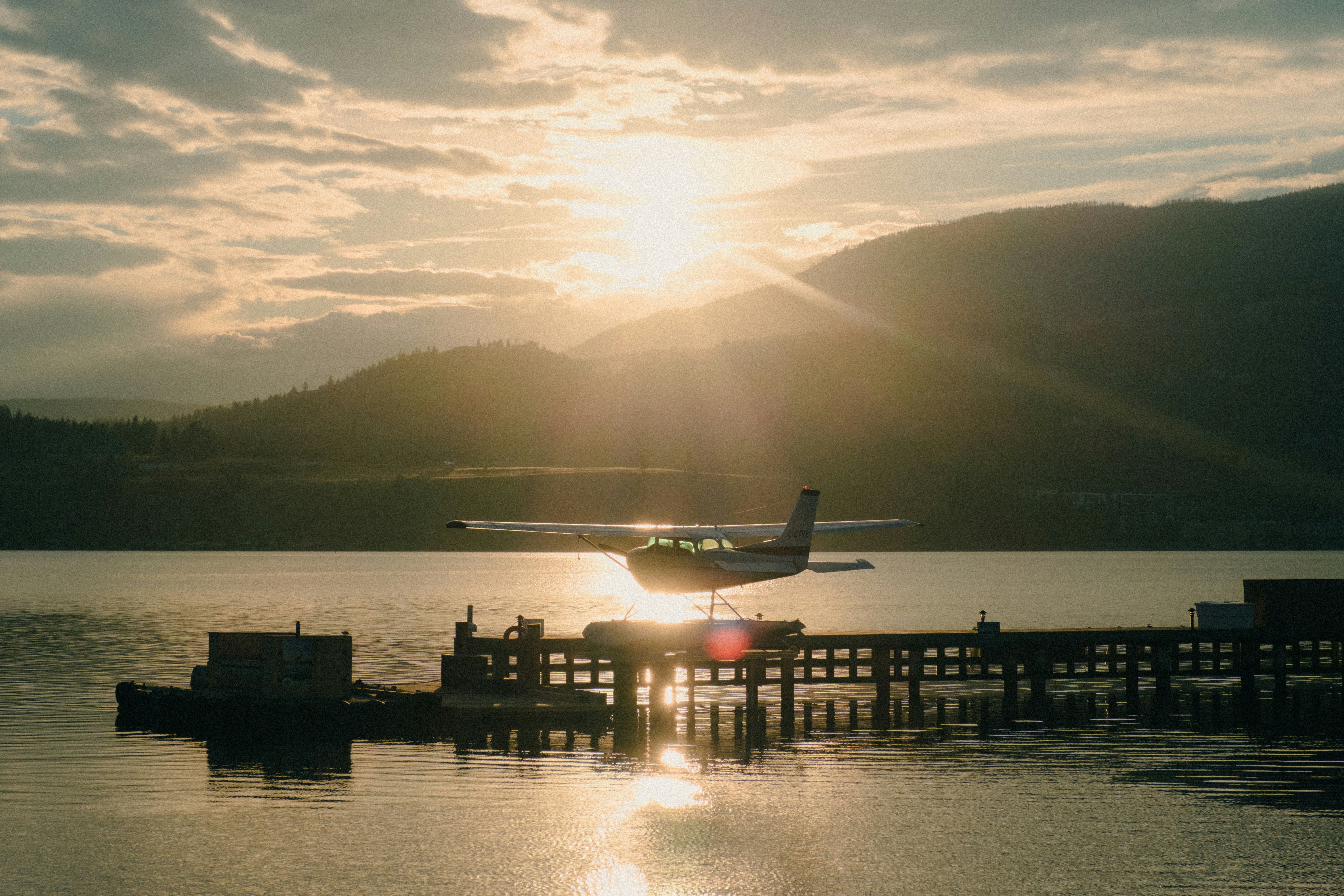 Hidroavión aterrizando en el agua al atardecer con montañas.