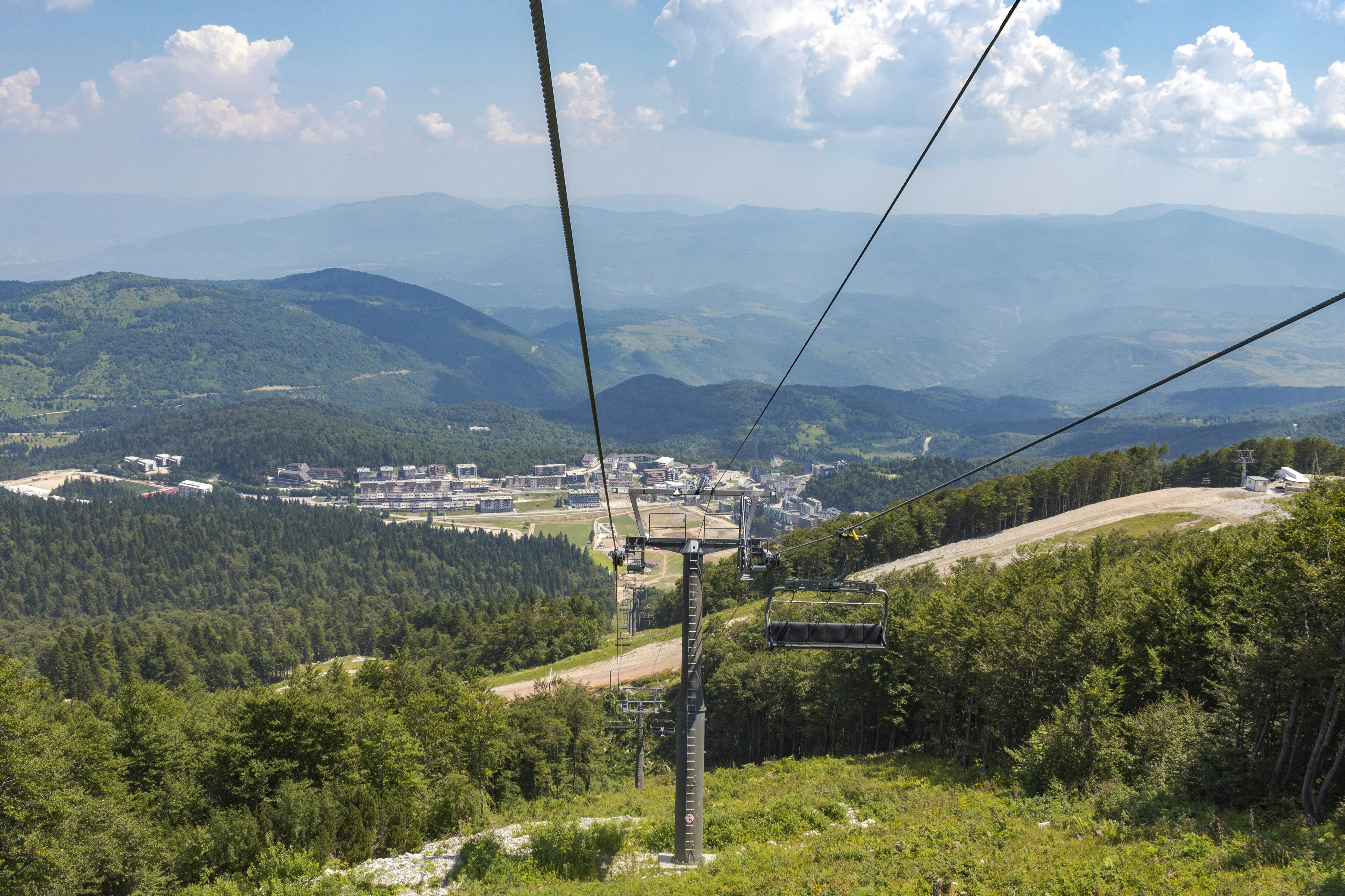Ski lift ascending a green mountain with village below.